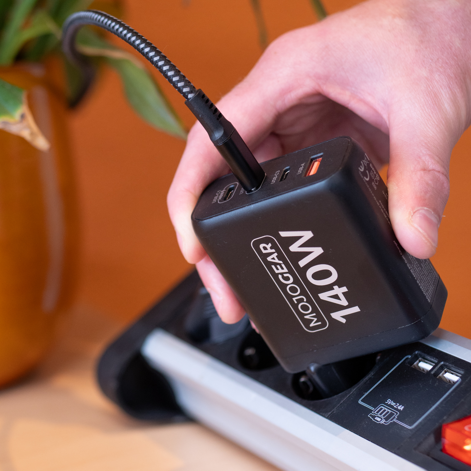 Zwarte voedingsadapter die een apparaat oplaadt. Tekst op adapter zegt 140W, aangesloten op stekkerdoos.