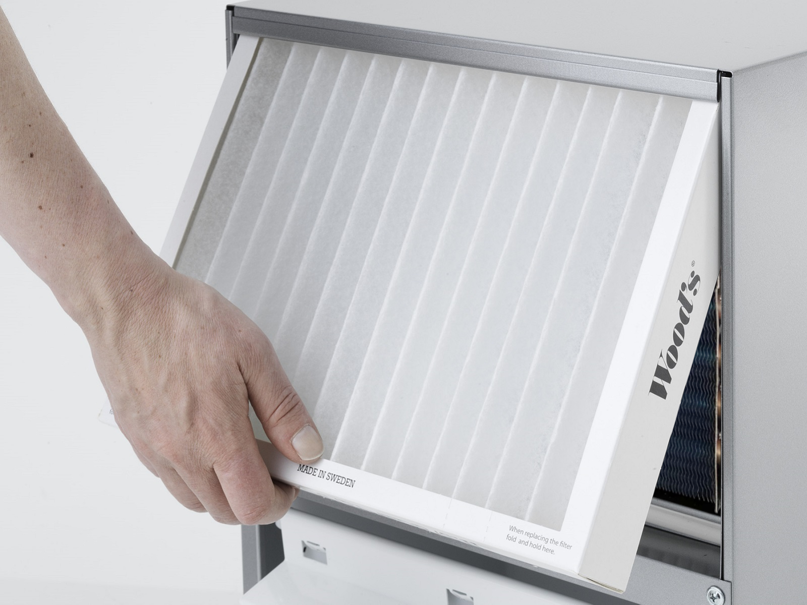Hand hält einen weißen Luftfilter aus einer Maschine. Filter ist mit 'Made in Sweden' beschriftet.