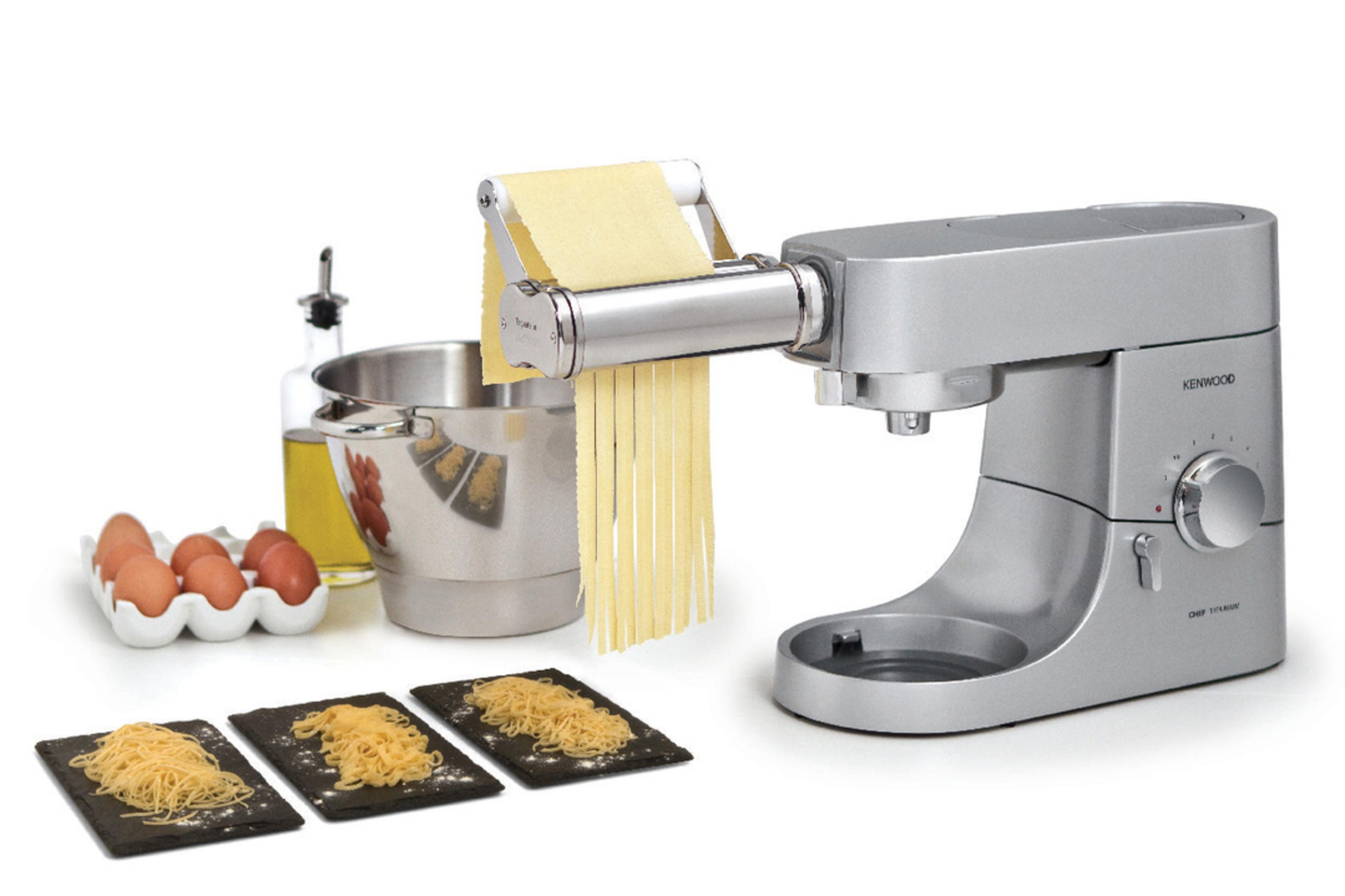 Un mixer da cucina Kenwood argentato con un accessorio per fare la pasta. Si stanno facendo gli spaghetti.