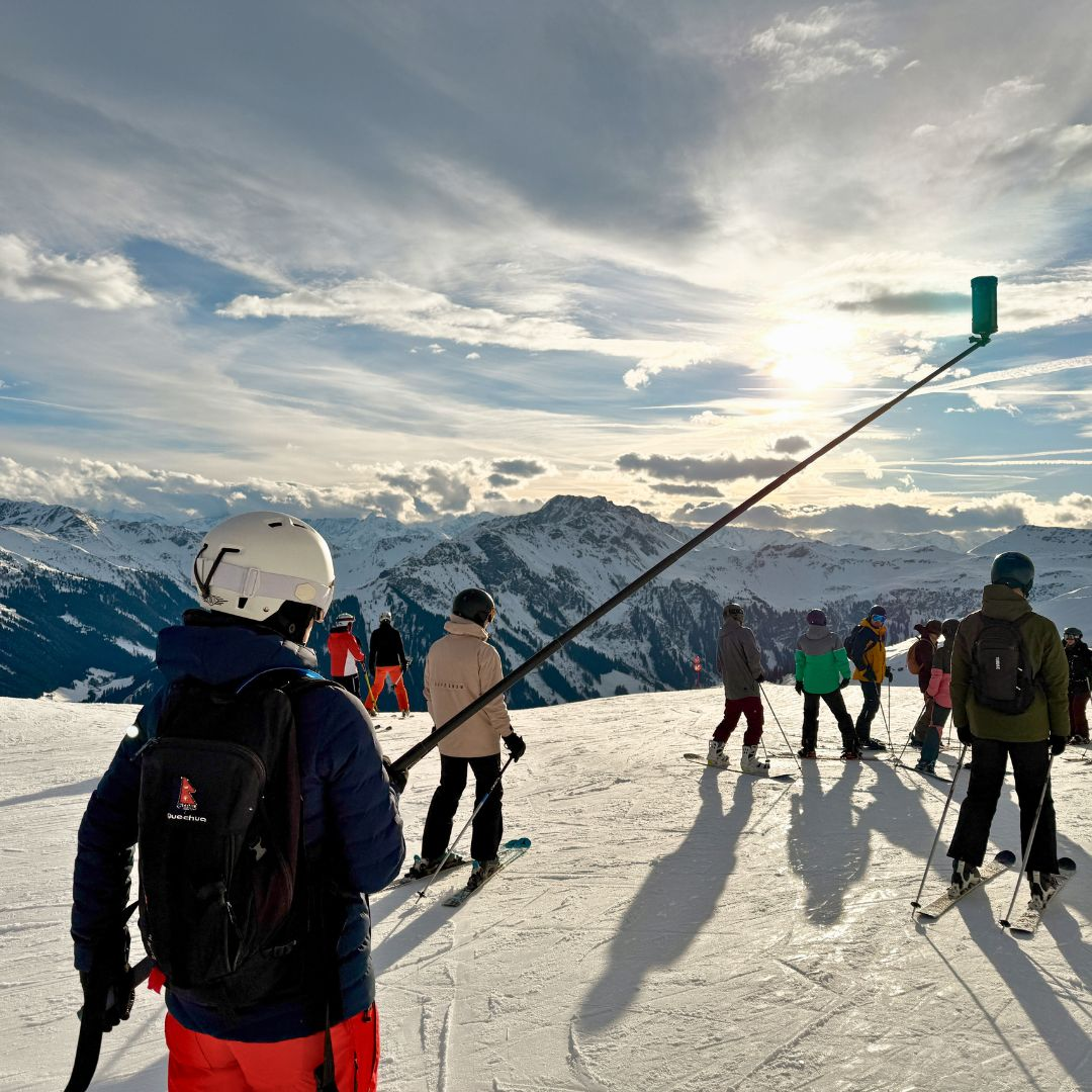 Skiërs op een besneeuwde berghelling met een lange camerakraan en een zonnige hemel op de achtergrond.