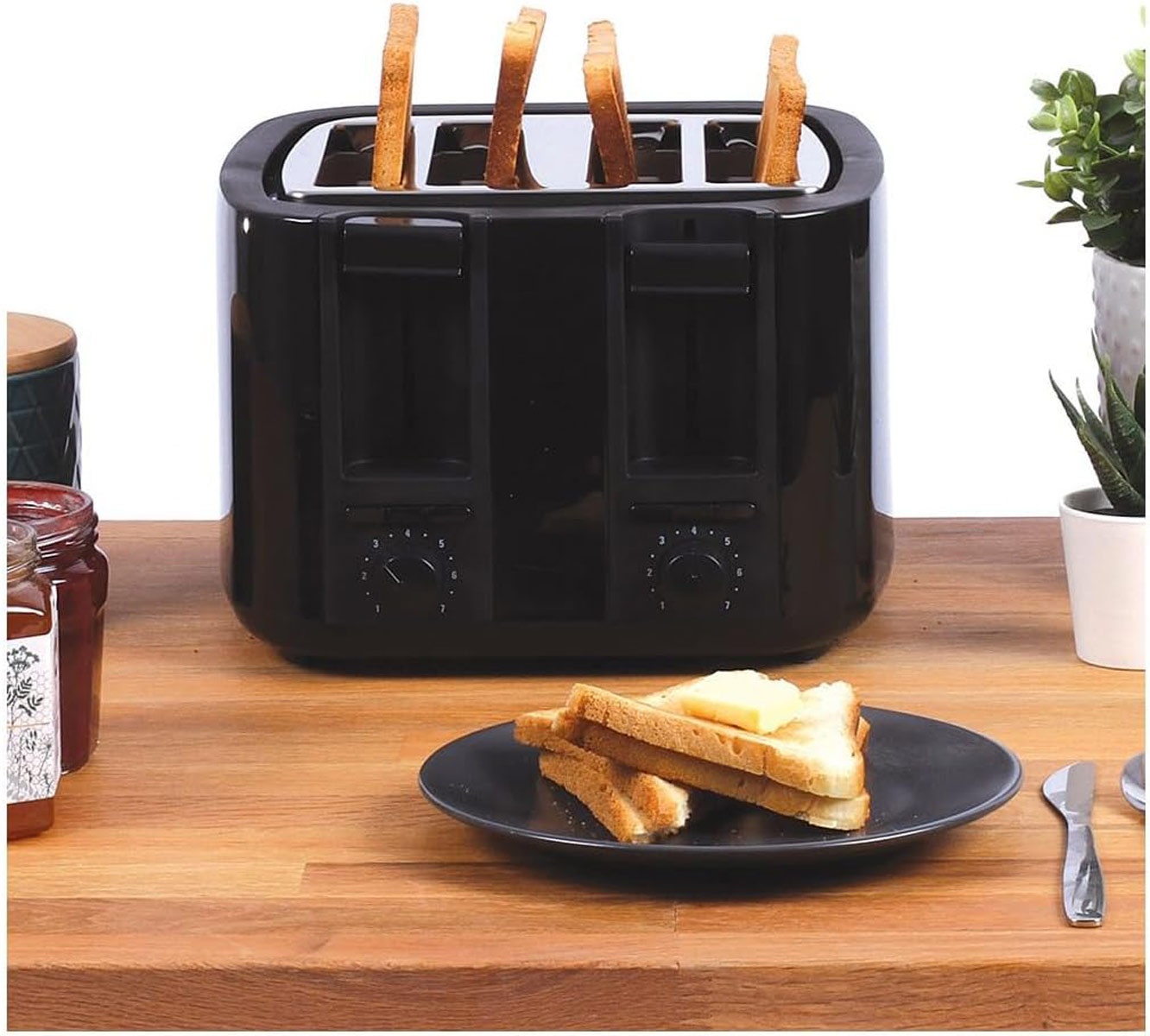 Schwarzer Toaster mit vier Schlitzen, Toast, Butter und Holzoberfläche sind sichtbar.
