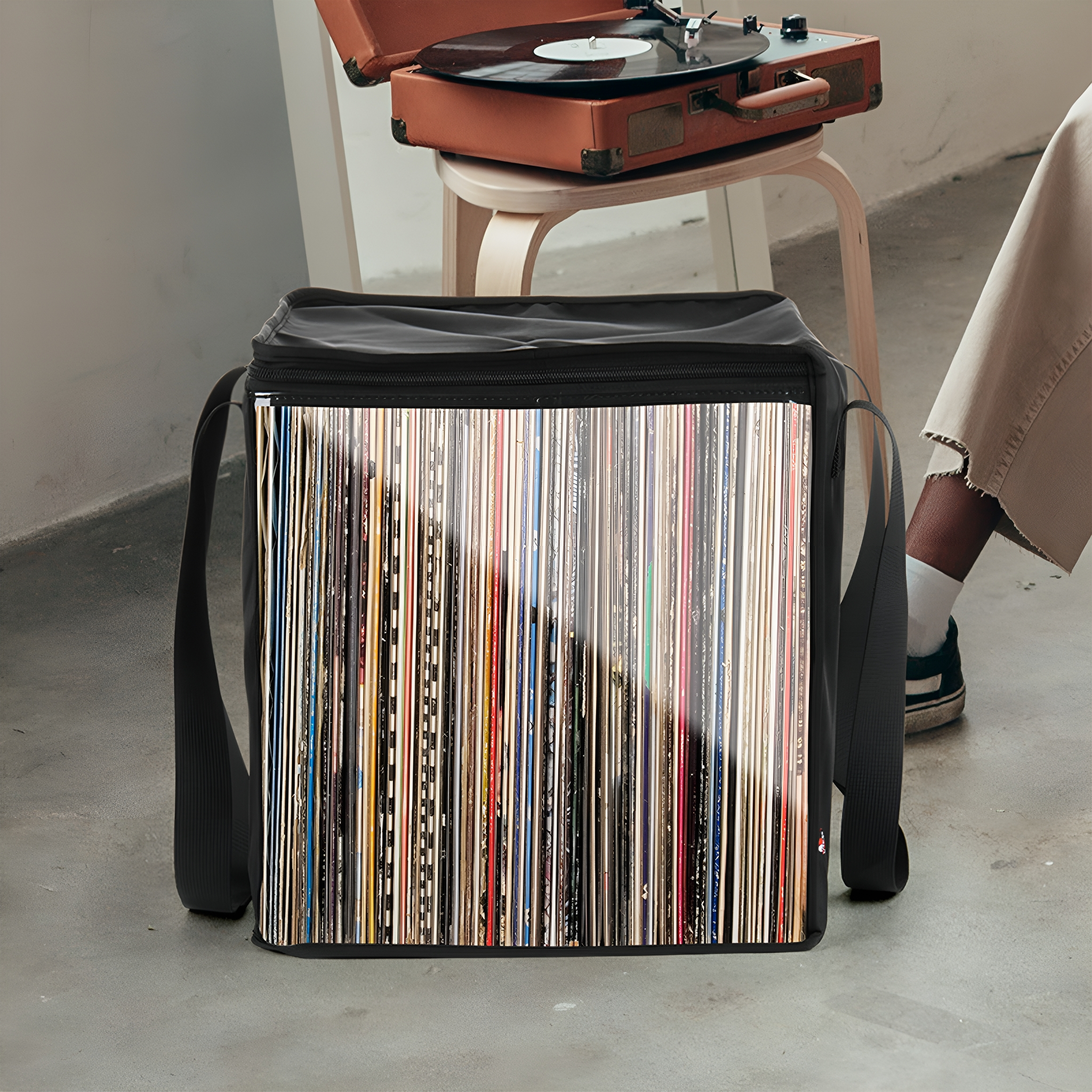 Schwarze Schallplattentasche gefüllt mit Schallplatten, im Hintergrund ein Plattenspieler und Hocker.