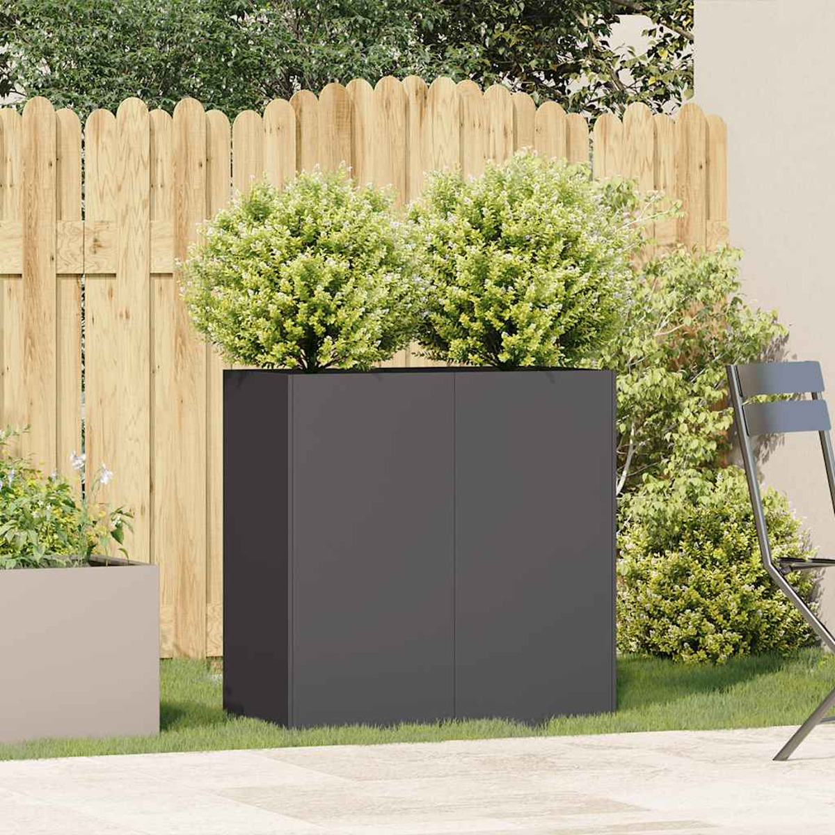 Fioriera grigio scuro con cespugli verdi. Recinzione in legno e una sedia sullo sfondo.