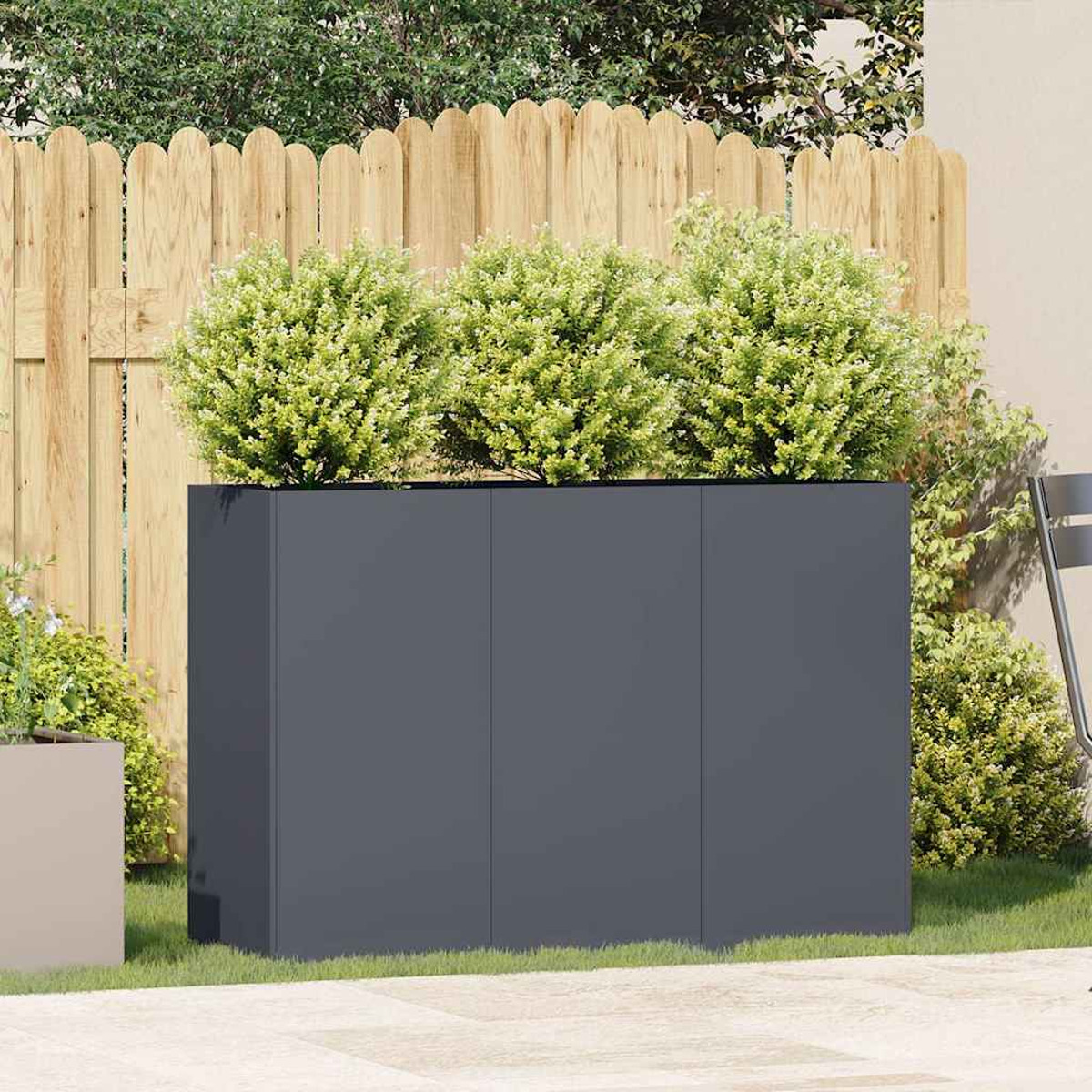 Una fioriera grigio scuro con tre cespugli verdi sopra, in un giardino, con una recinzione.