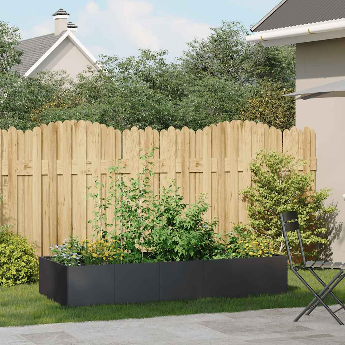 Fioriera grigio scuro con piante in un giardino, con una staccionata in legno e una casa sullo sfondo.