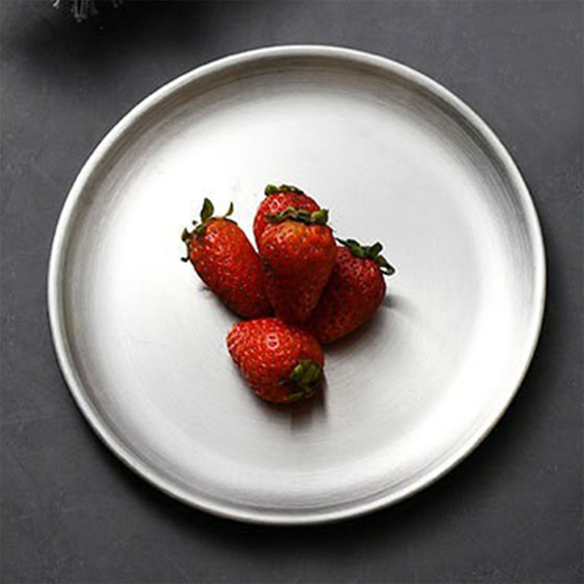 Ein weißer Teller mit Erdbeeren, vier rote Beeren auf weißem Grund, dunkler Hintergrund.