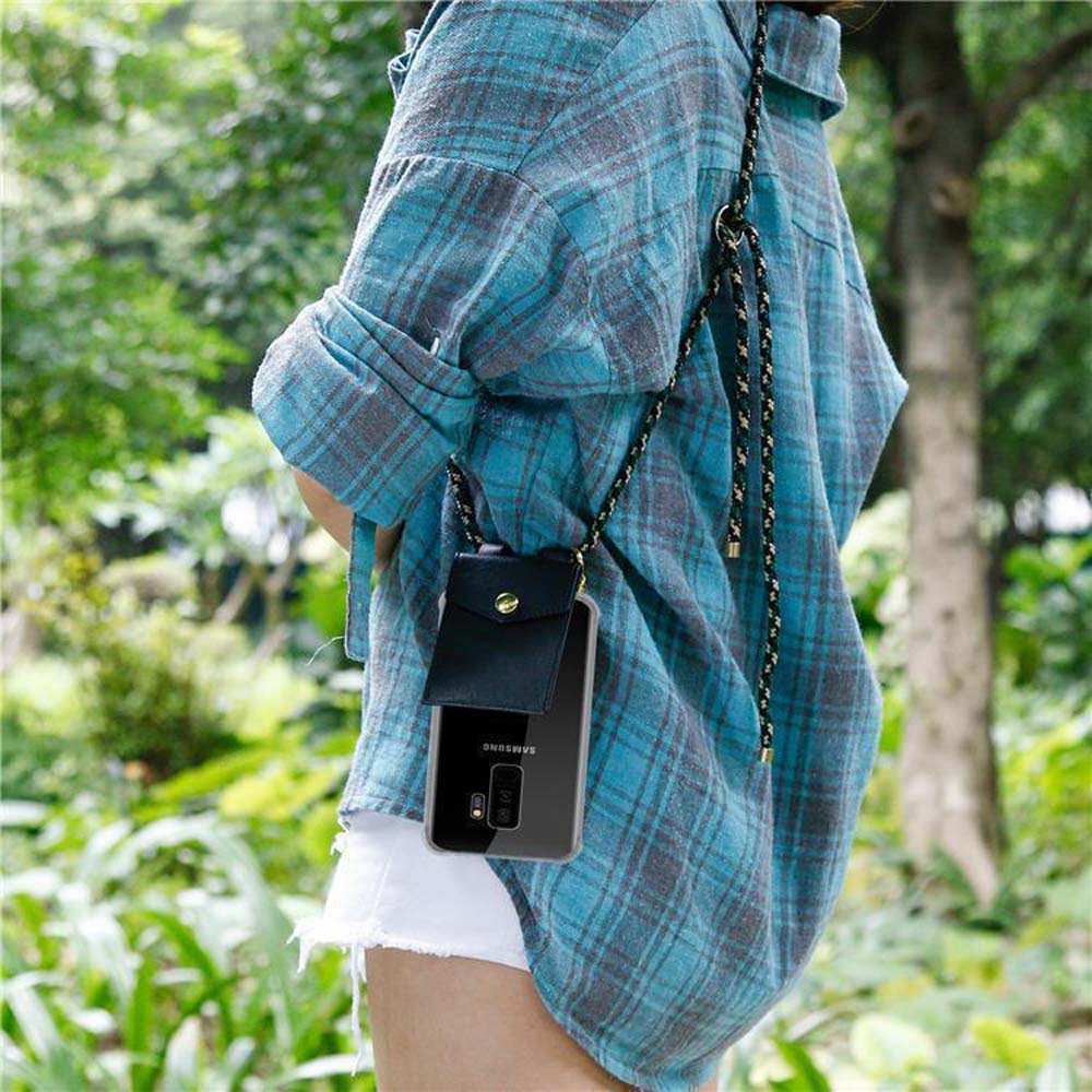 Persona con camicia a quadri blu e pantaloncini bianchi. Una custodia nera per telefono è appesa al collo.