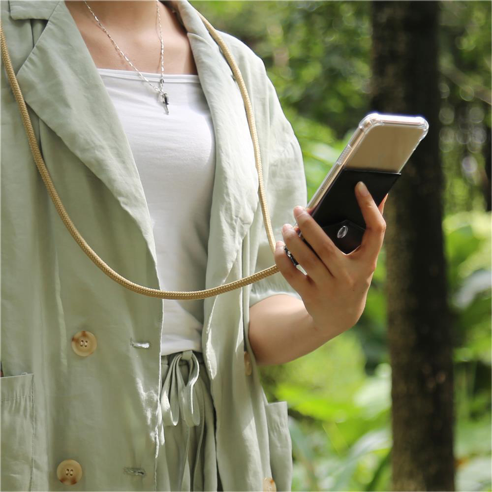 Donna che tiene in mano un telefono con un cordino. Il telefono ha un'impugnatura nera. Lo sfondo è una foresta verde sfocata.