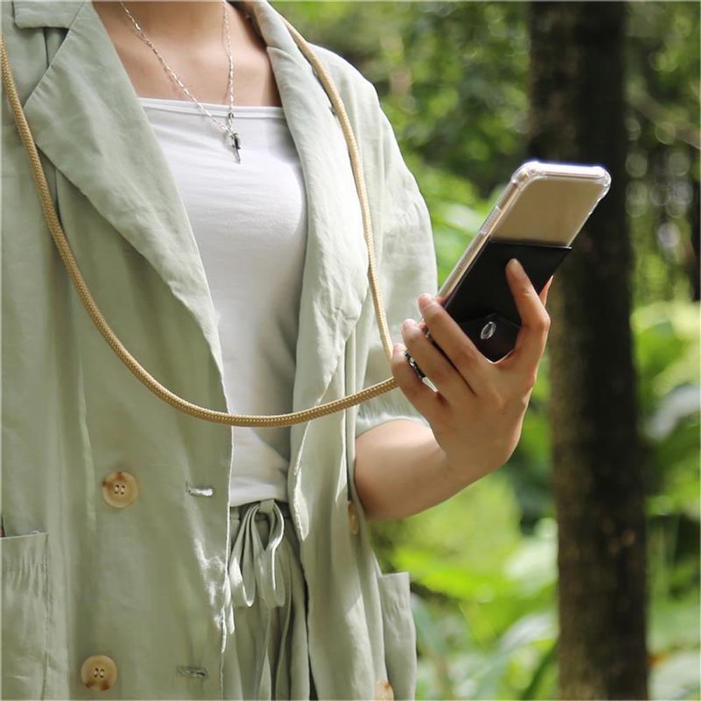 Donna con cappotto verde, collana beige, che tiene un telefono con custodia nera e un'impugnatura.