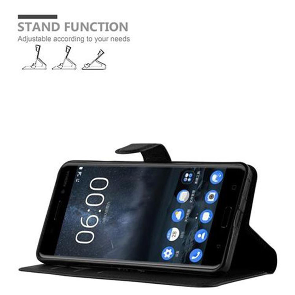 Telefon in einer Hülle steht auf. Die Hülle ist schwarz. Text oben sagt 'Standfunktion'. Die Uhrzeit ist 06:00.