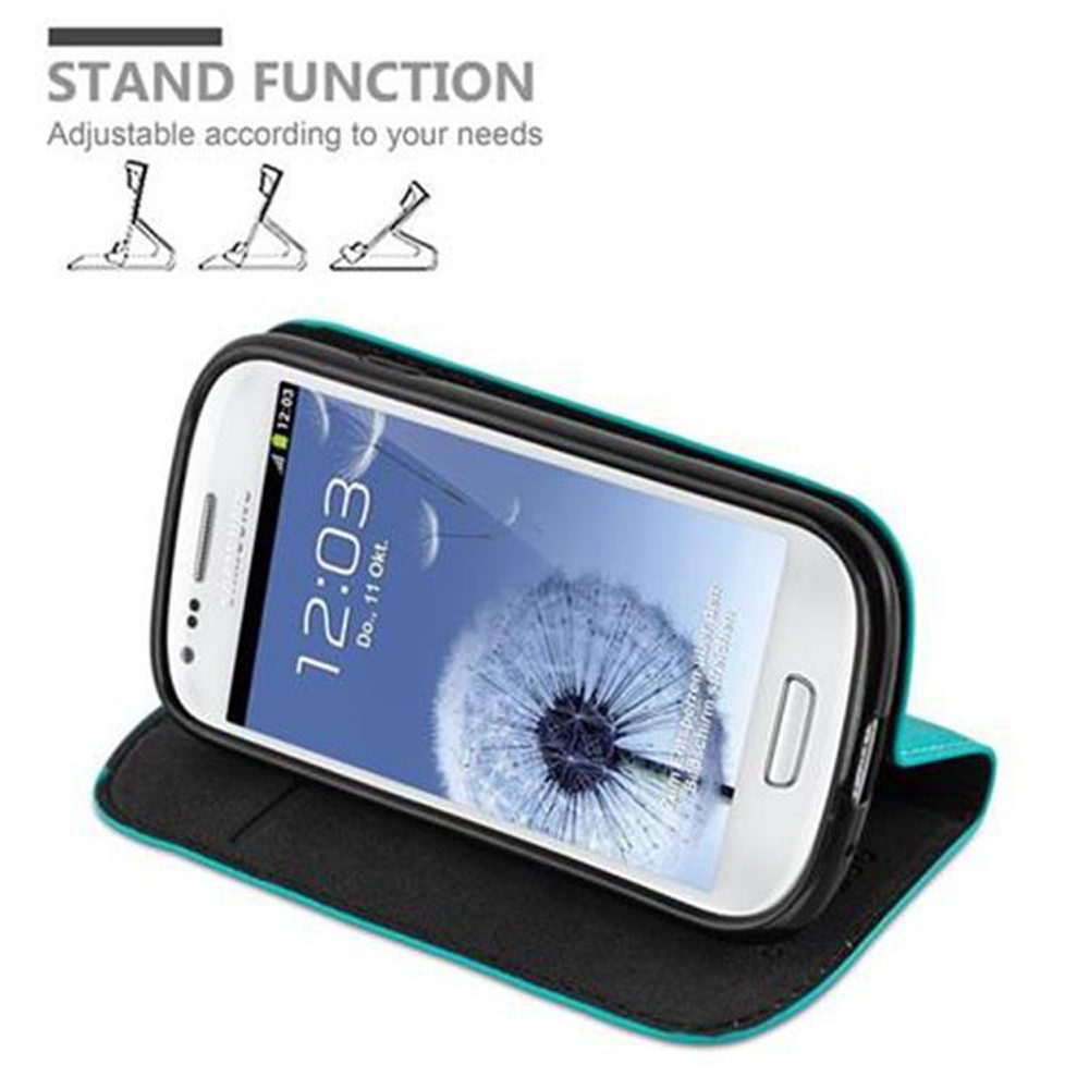 Teléfono blanco en una funda con soporte. El teléfono muestra la hora. Texto: Función de soporte. La funda es turquesa y negra.
