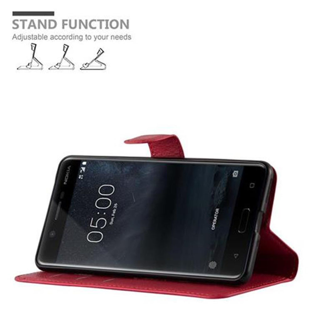 Telefon in roter Hülle, in Standposition. Das Telefon zeigt die Uhrzeit und das Datum an.