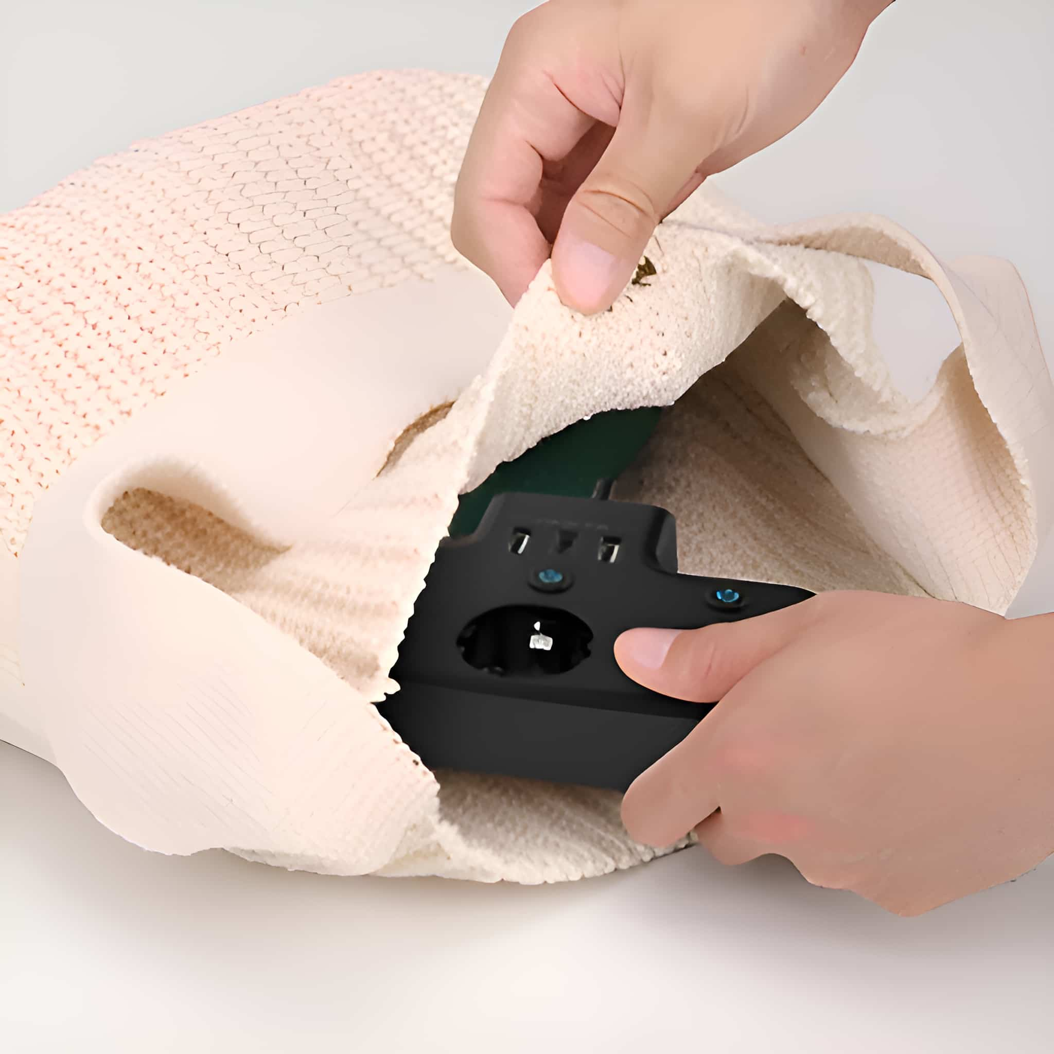 Hände, die eine schwarze Steckdosenleiste aus einer beigen Handtasche nehmen.