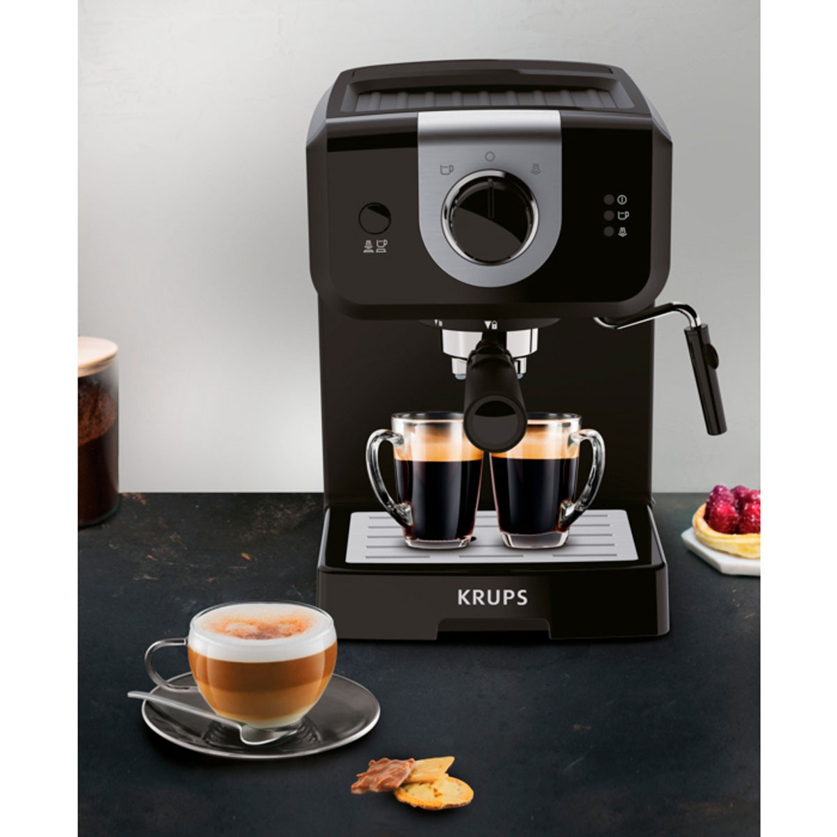 Una cafetera negra con dos tazas de café y un latte macchiato al lado.