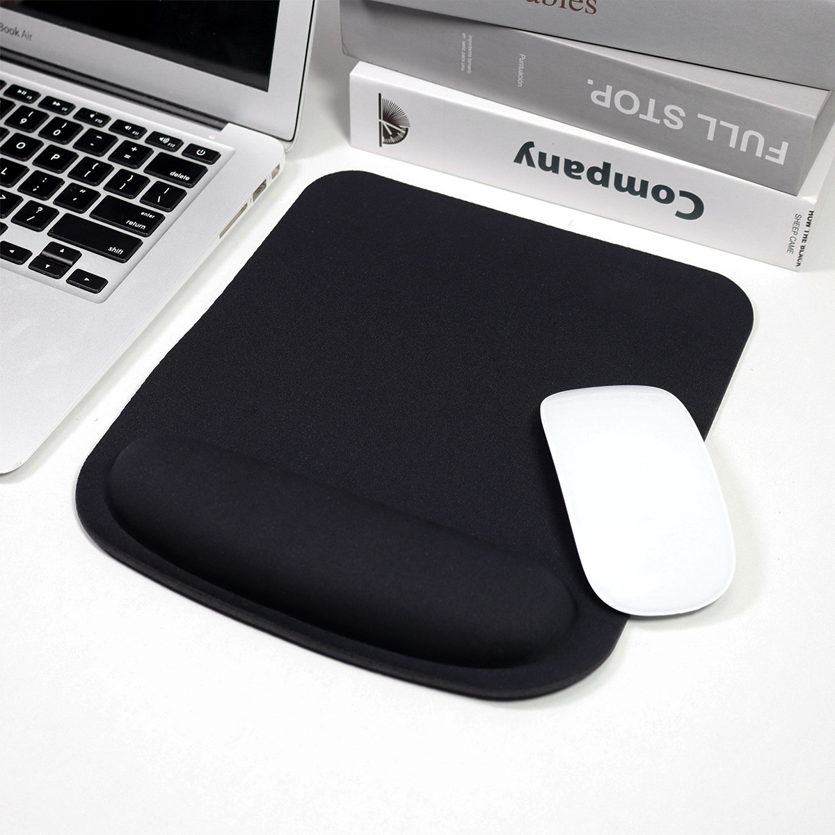 Zwarte rechthoekige muismat met polssteun. Een laptop en witte muis op de tafel.