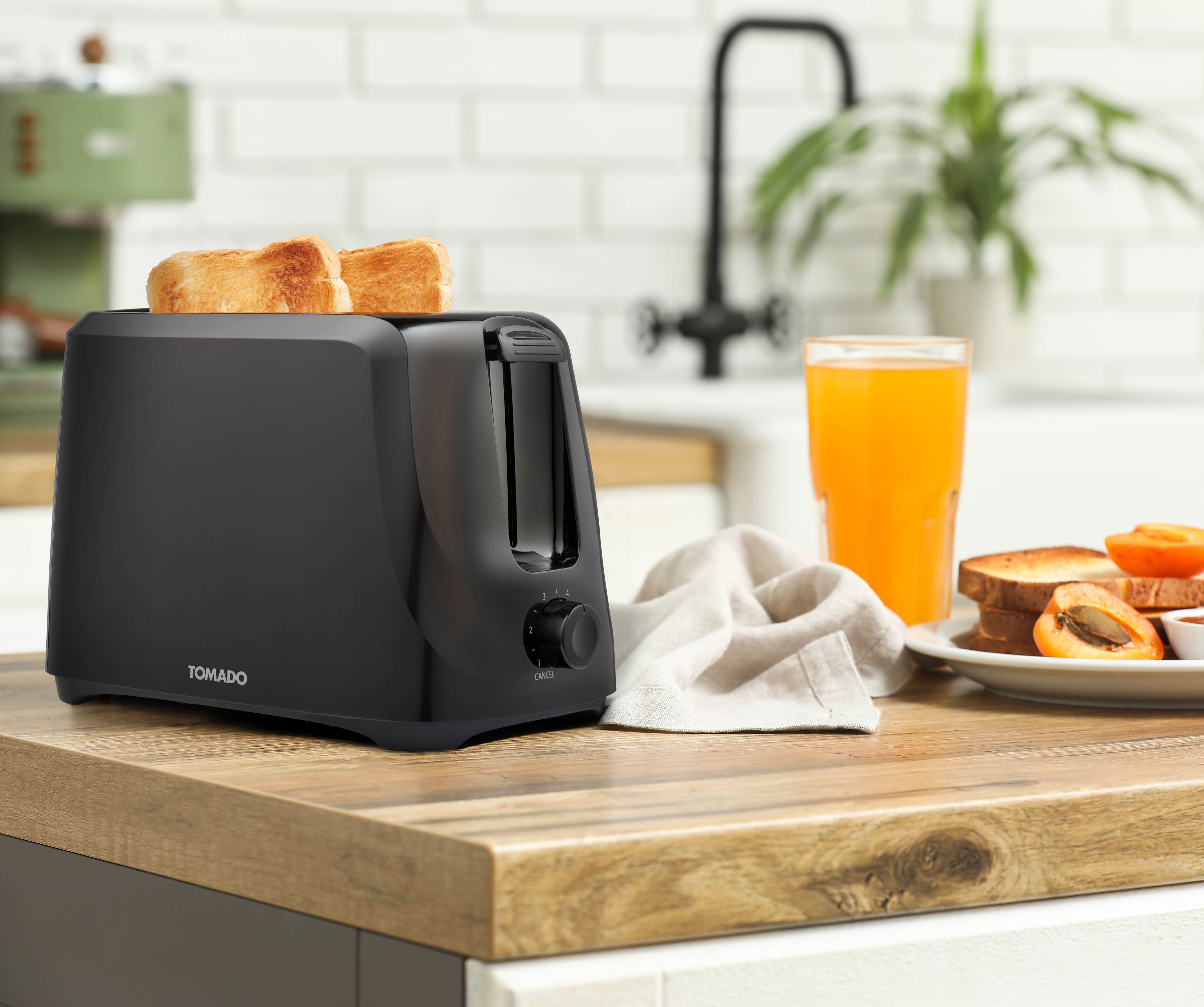 Black toaster with two slices of toast on a wooden countertop next to a glass of orange juice.