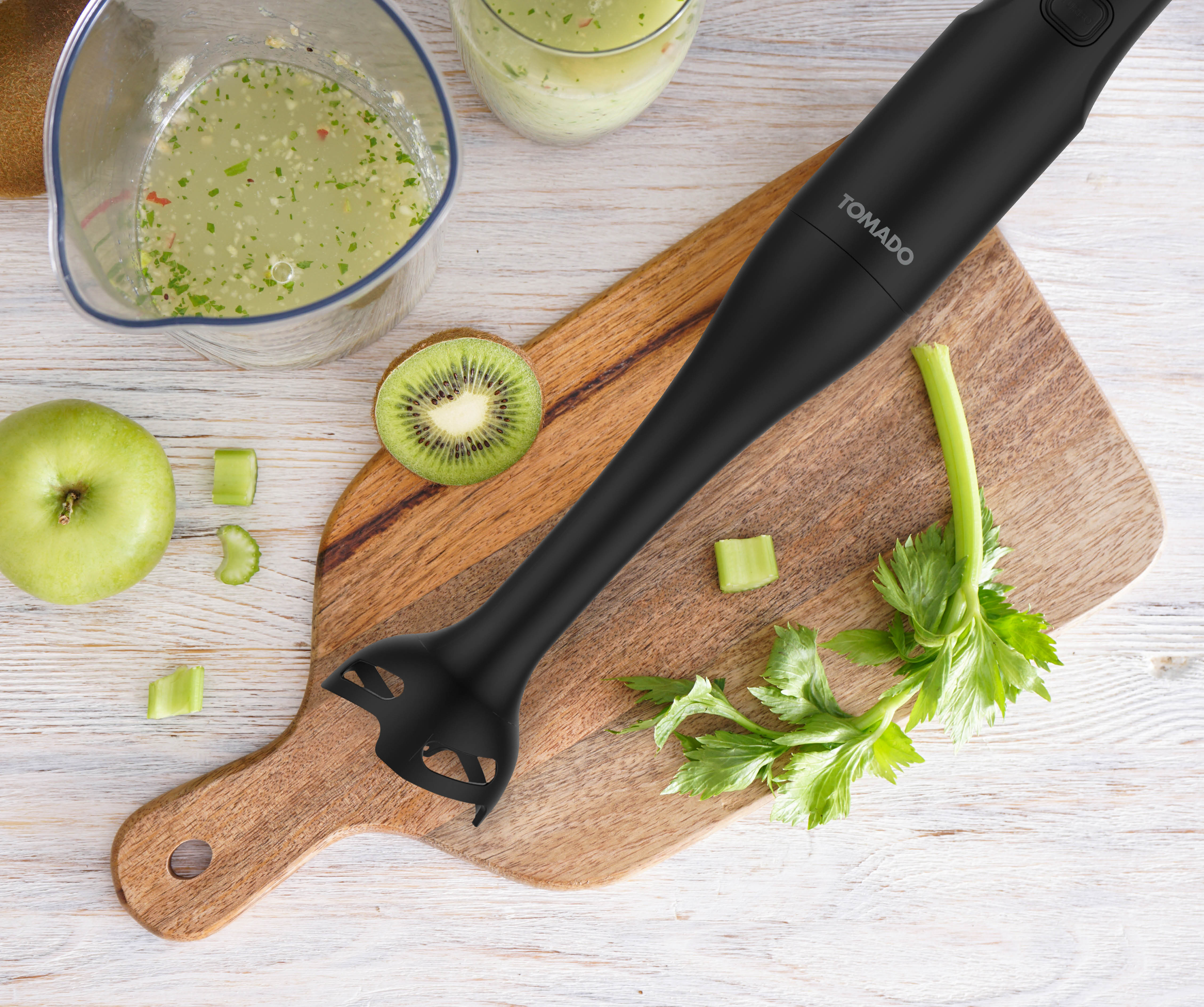 Zwarte staafmixer met ingrediënten: kiwi, groene appel, selderij, op een houten snijplank.