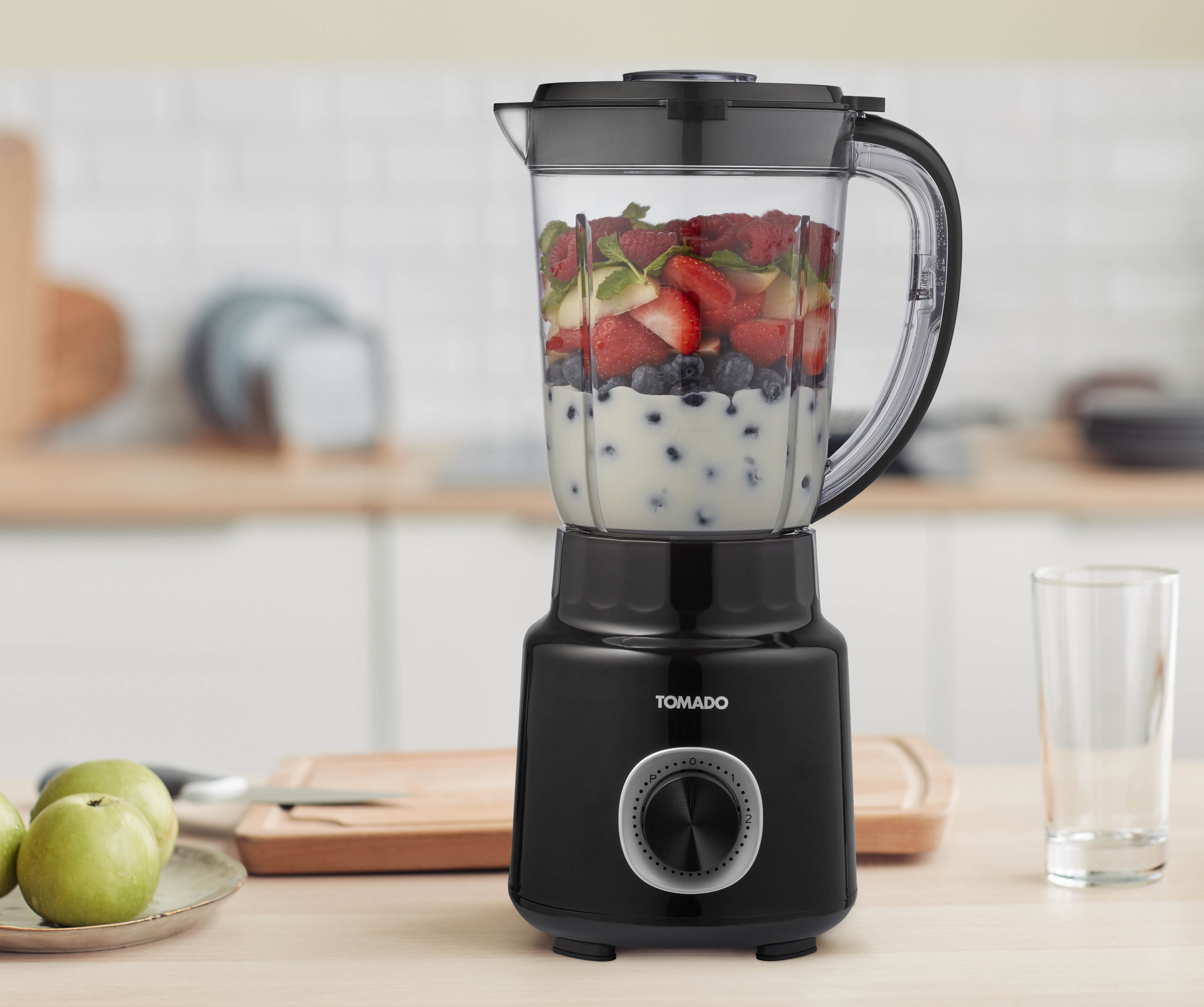 Black blender with a clear pitcher filled with fruit and a white liquid, on a wooden counter.
