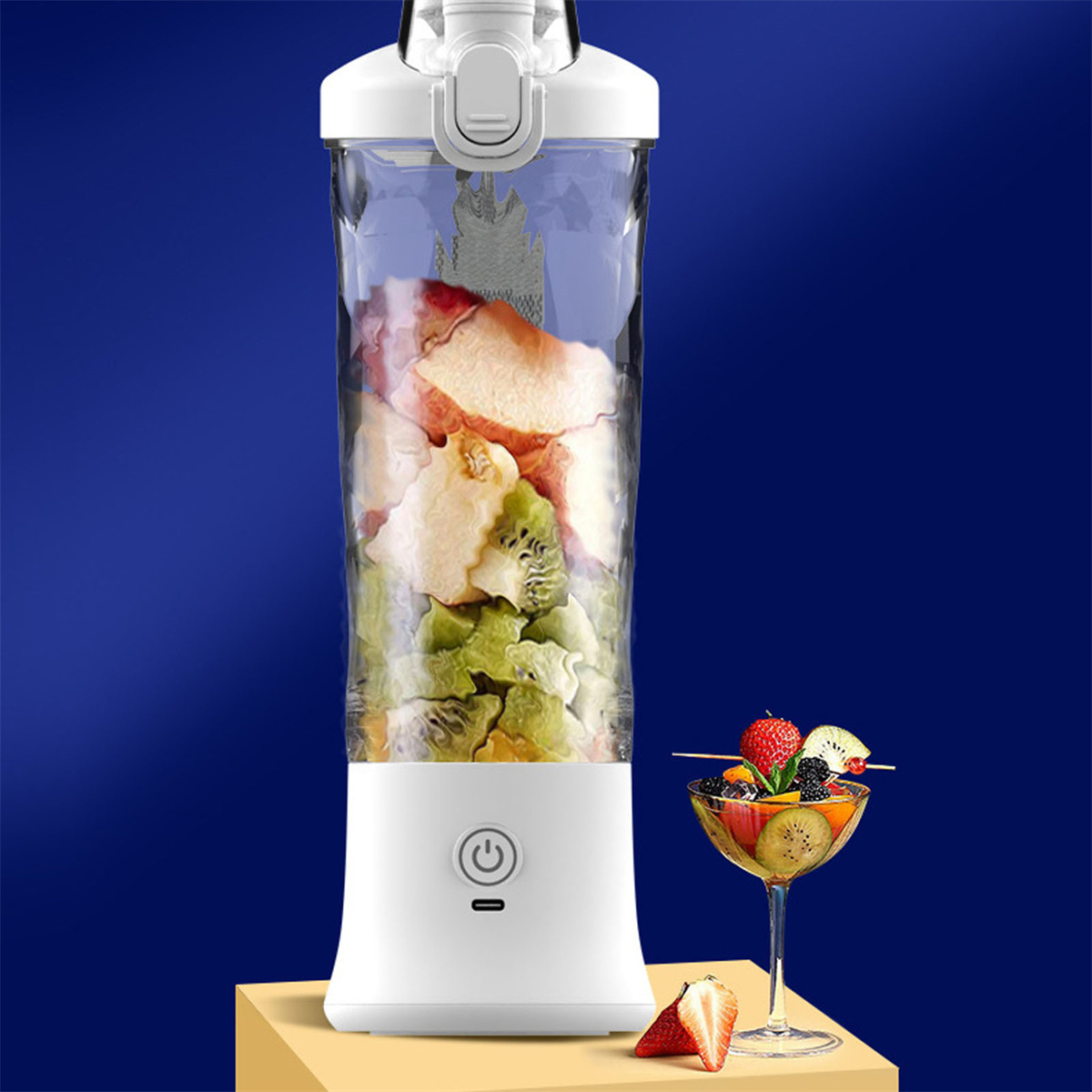 Weißer Mixer mit Früchten, und ein Obstcocktail daneben, auf blauem Untergrund.