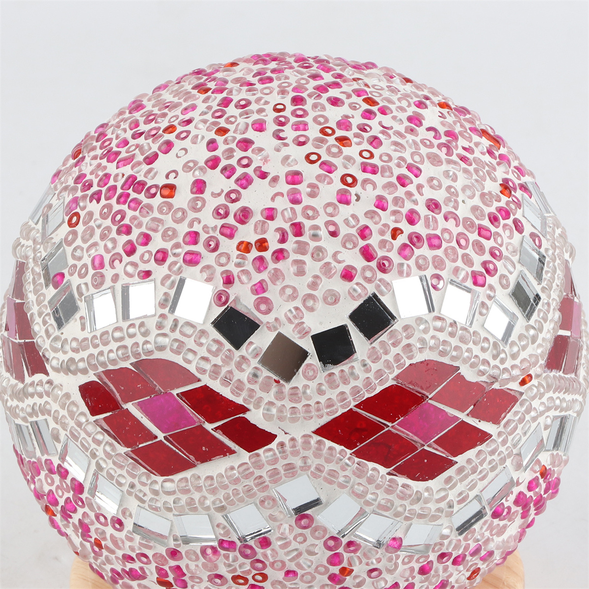 Mosaikglaskugel mit rosa und roten Akzenten. Spiegelflächen bilden ein Muster, weißer Sockel.