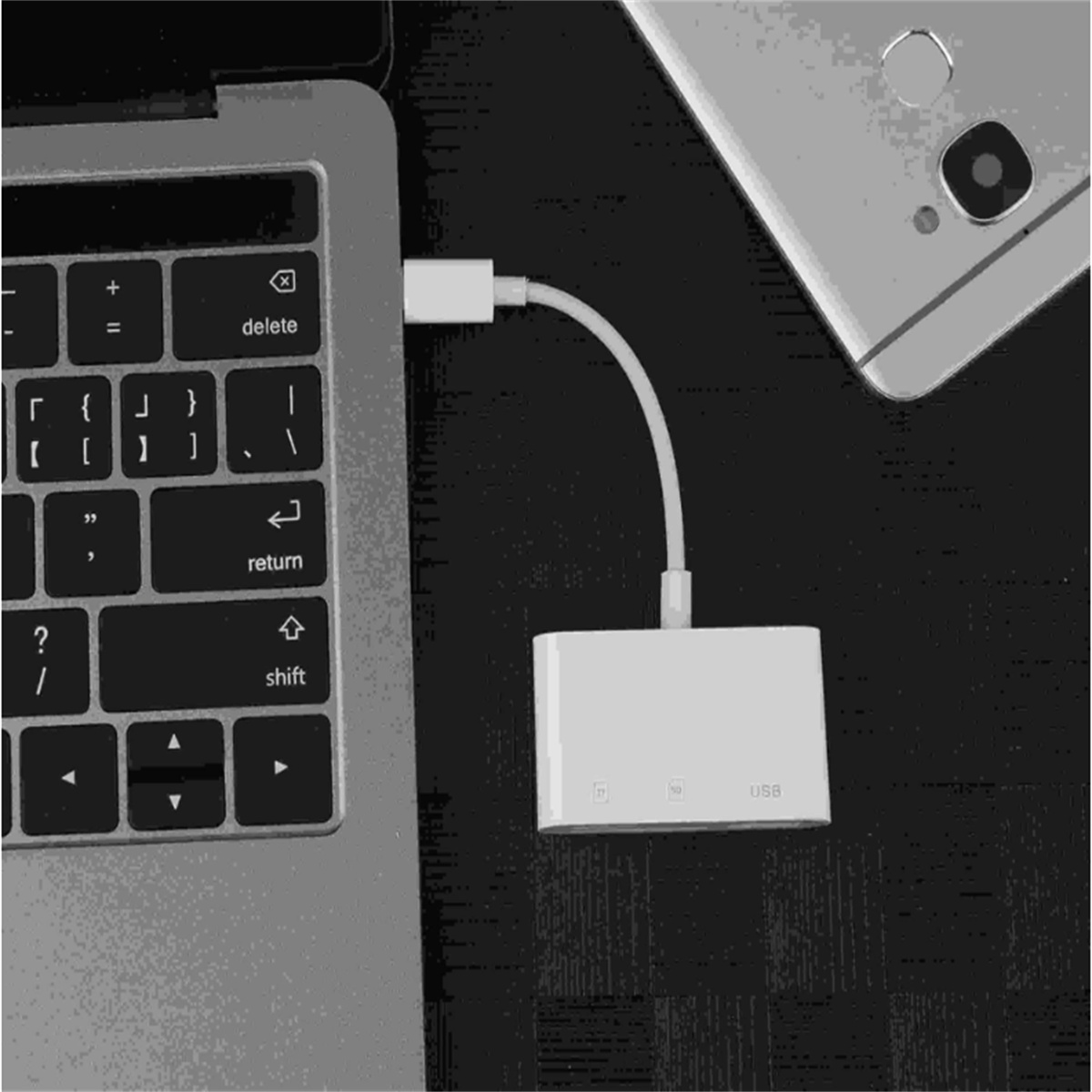Laptop mit weißem USB-Adapter verbunden. Ein Telefon befindet sich neben dem Laptop. Schwarzer Hintergrund.