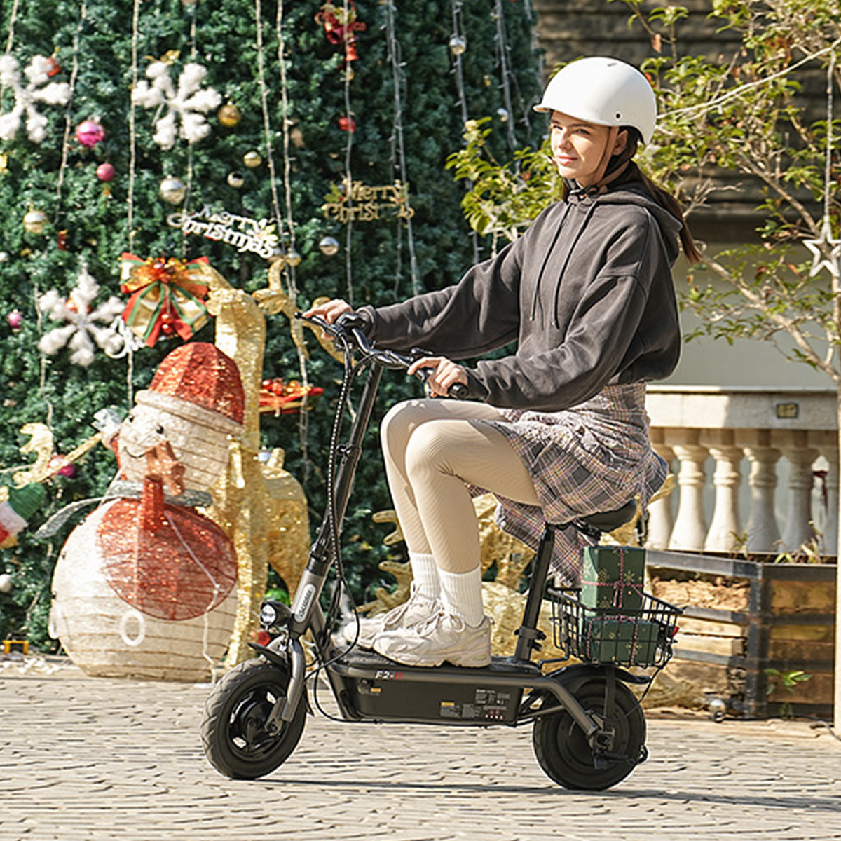 Kobieta na skuterze elektrycznym, w kasku, obok choinki.