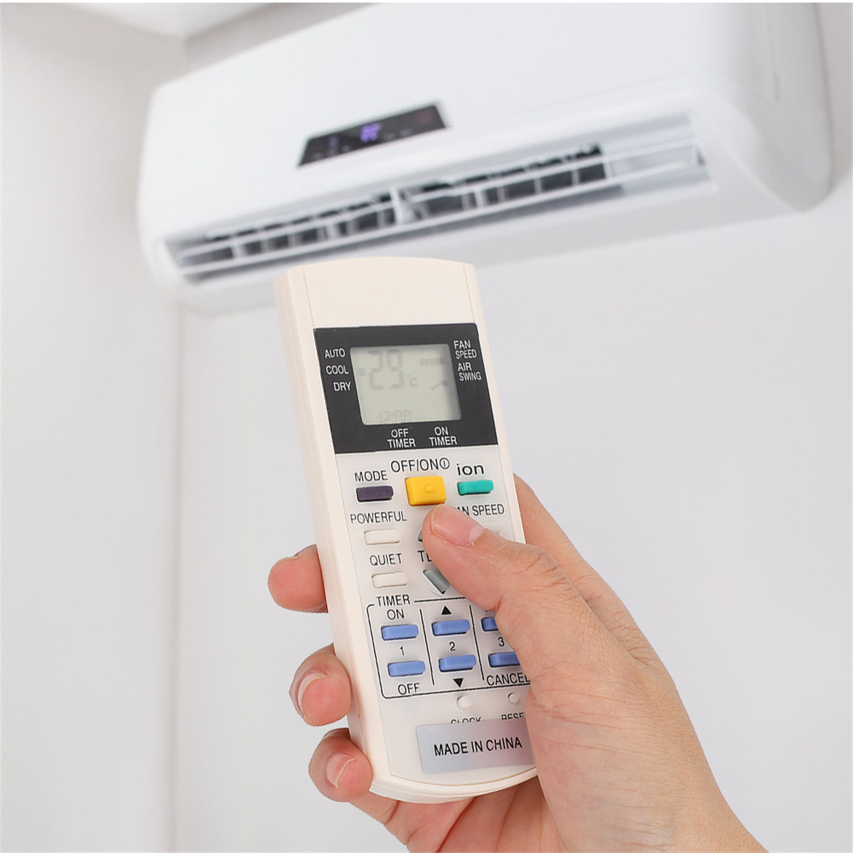 Hand hält eine weiße Fernbedienung, die auf eine Klimaanlage gerichtet ist.