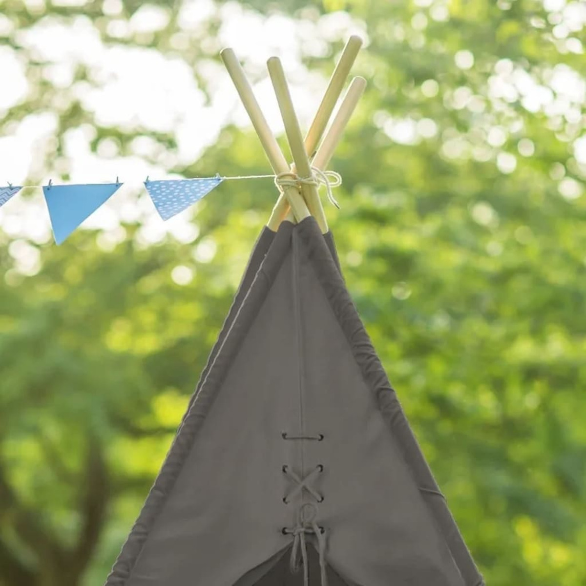 Ein graues Tipi-Zelt mit Holzpfählen und einer Schnur mit blau-weißen Flaggen.