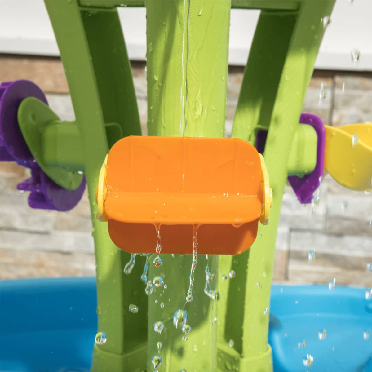 Ein Wasserspieltisch mit grünem Sockel und orangen Elementen. Wasser fließt aus orangen Elementen.