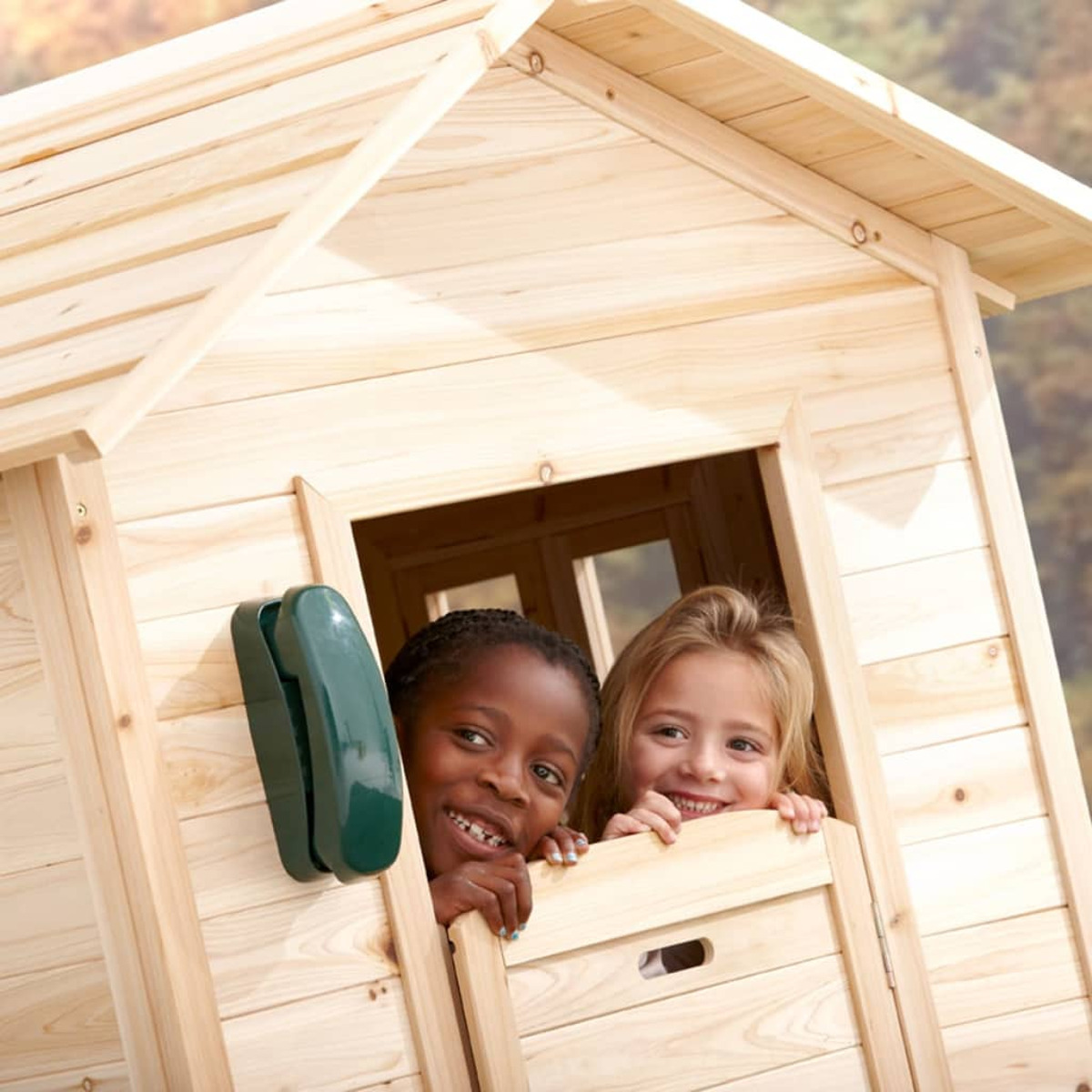 Zwei Kinder schauen aus einem Fenster eines Spielhauses aus Holz. Eines ist schwarz, das andere weiß.