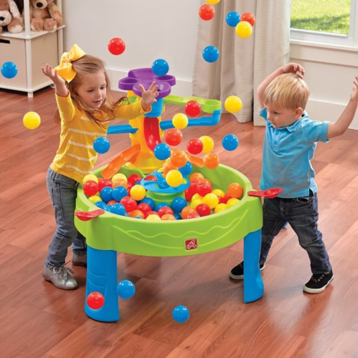 Zwei Kinder spielen mit einem Bällchenbadtisch und werfen Bälle in einem hellen Spielbereich.
