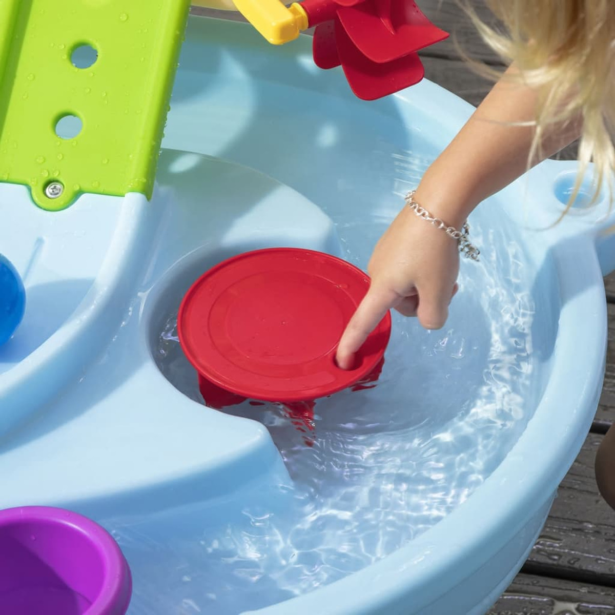 Ein Kinderhand zeigt auf ein rotes Wasserrad in einem blauen Wassertisch mit Wasser.
