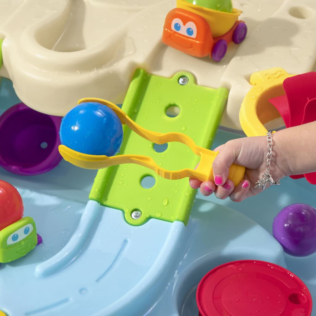 Die Hand eines Kindes mit Armband spielt mit einem blauen Ball in einem Wassertisch mit Spielzeug.