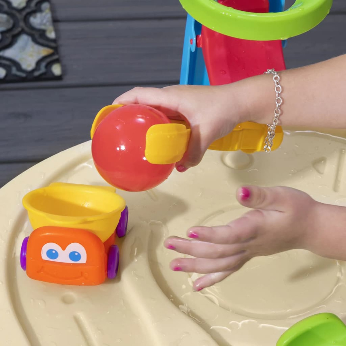 Kinderhände spielen mit einem Wassertisch, halten einen roten Ball mit gelben Griffen und ein Spielzeugauto.