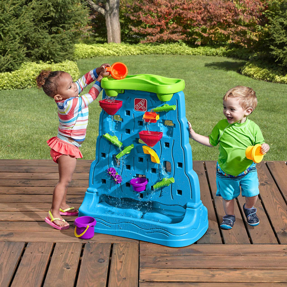 Zwei Kinder spielen mit einem blauen Wassertisch mit fließendem Wasser. Hintergrundeinstellung mit grünem Gras.