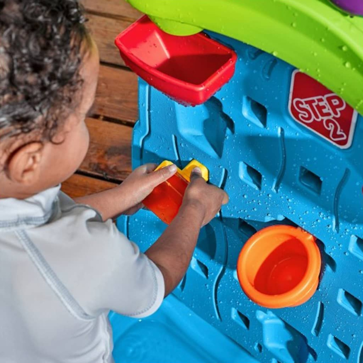 Ein Kind spielt mit einem Wasserspielzeug, blau mit orangefarbenen und grünen Elementen.
