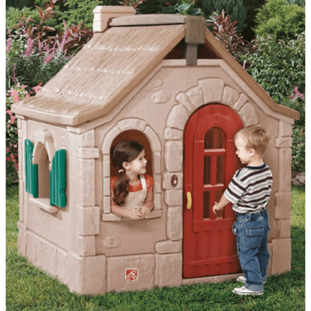 Ein Spielhaus mit zwei Kindern. Ein Kind schaut aus dem Fenster, ein anderes klopft an die rote Tür.