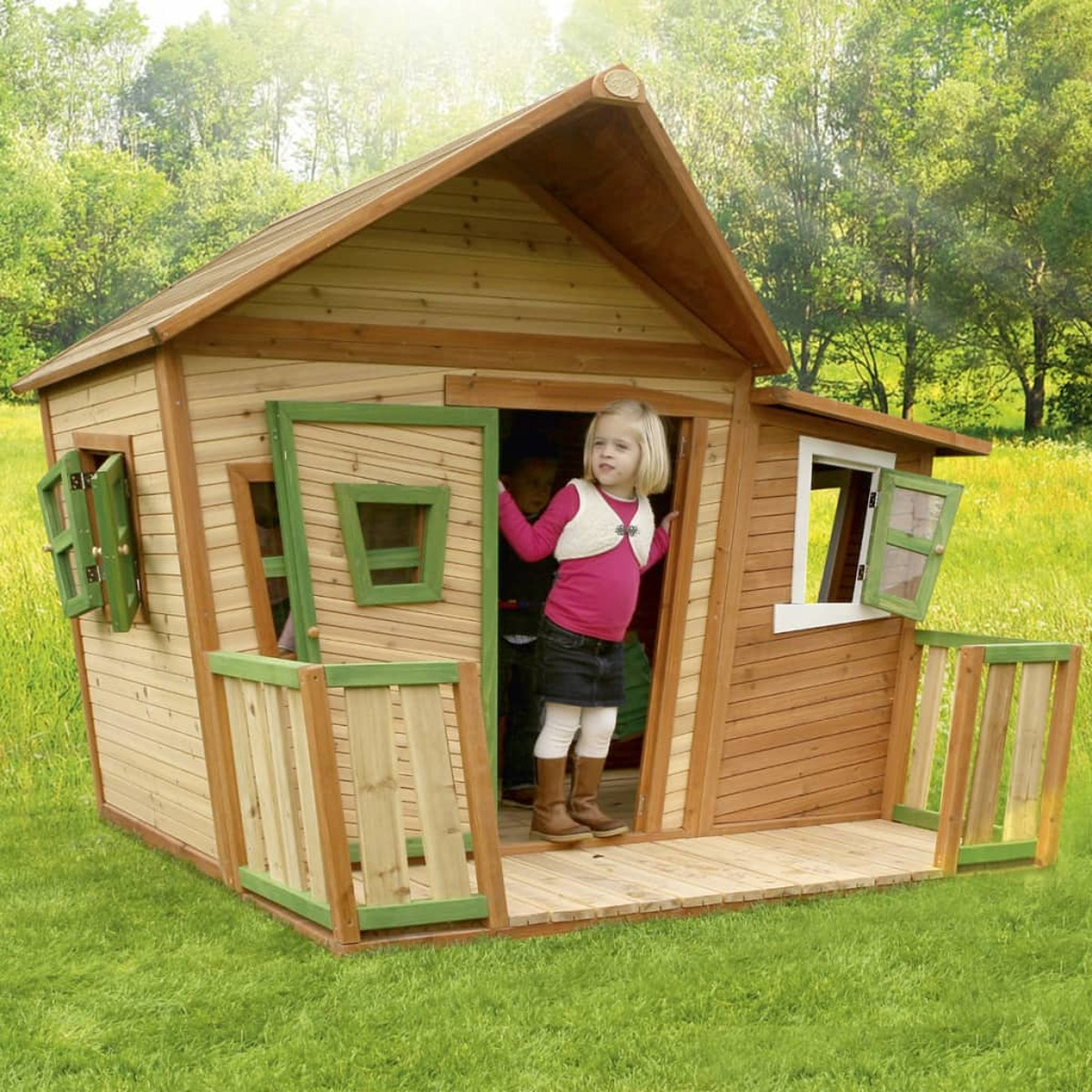 Ein hölzernes Spielhaus mit Kindern drinnen und auf der Veranda auf einer grünen Wiese.