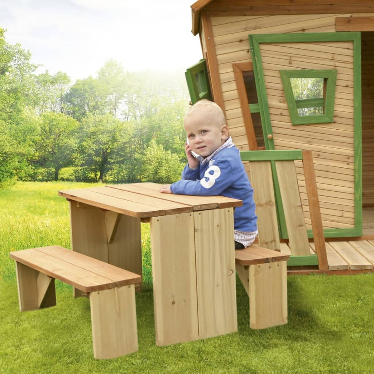 Junger Junge an einem Picknicktisch im Garten, in der Nähe eines Holzspielhauses.