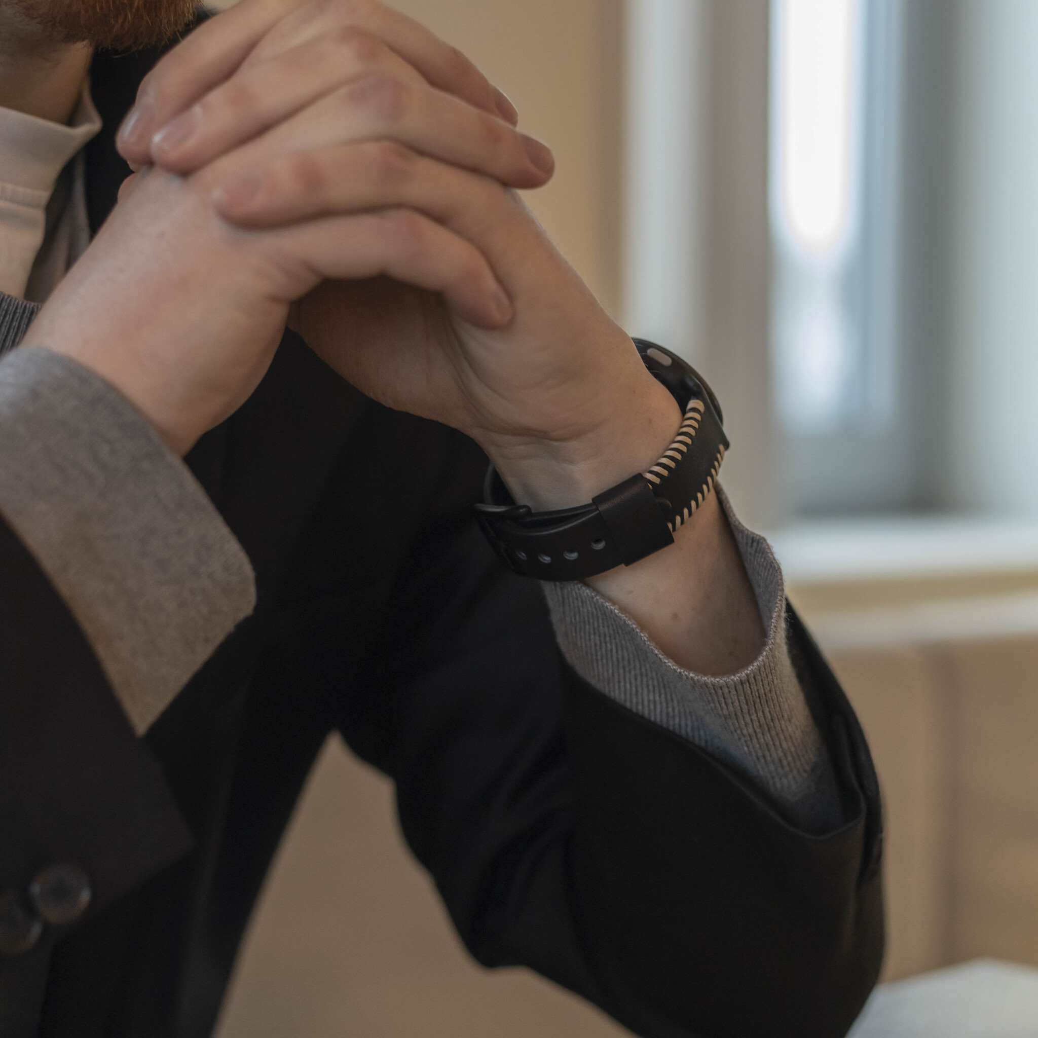Hände einer Person mit einem schwarzen und silbernen Smartband. Die Person trägt einen Blazer.