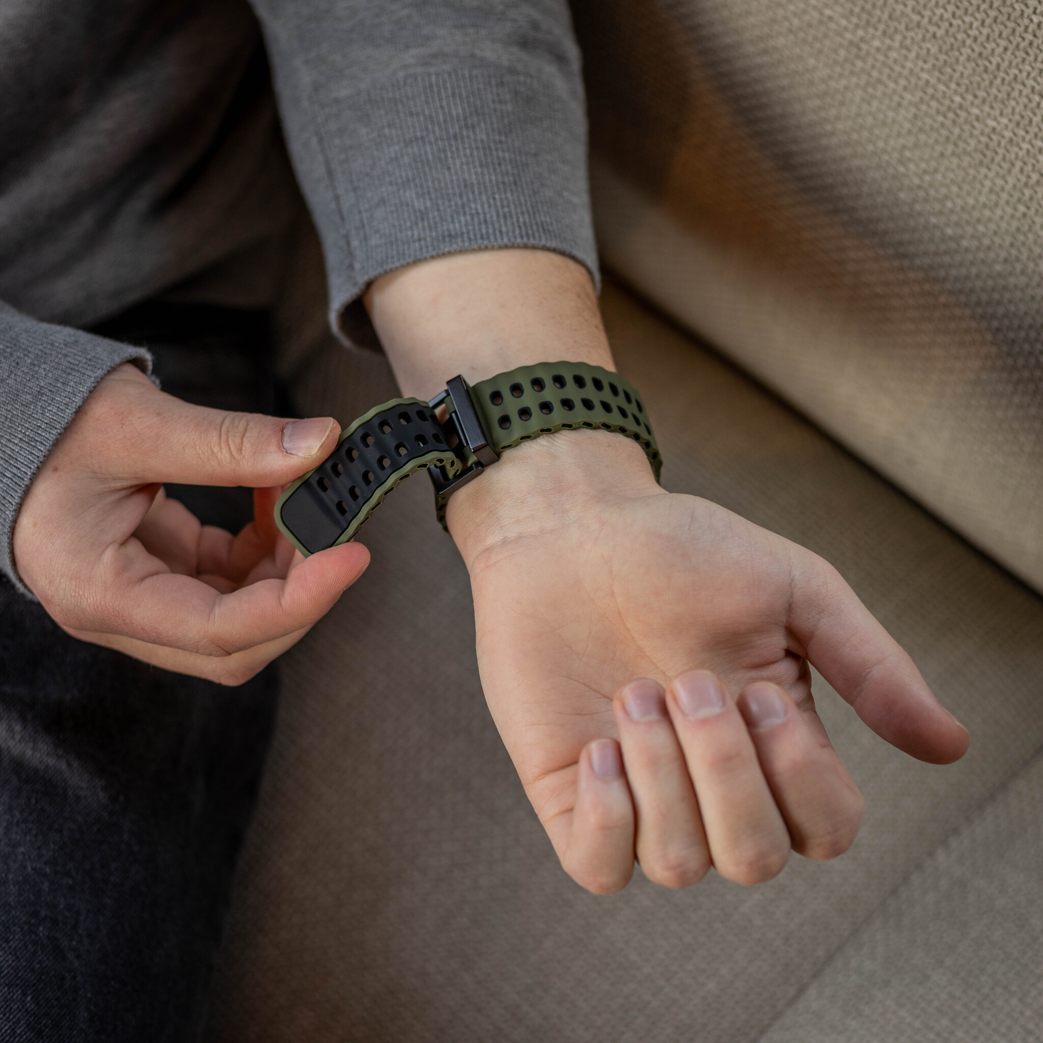 Eine Person, die ein olivgrünes und schwarzes Smartwatch-Armband am Handgelenk trägt.