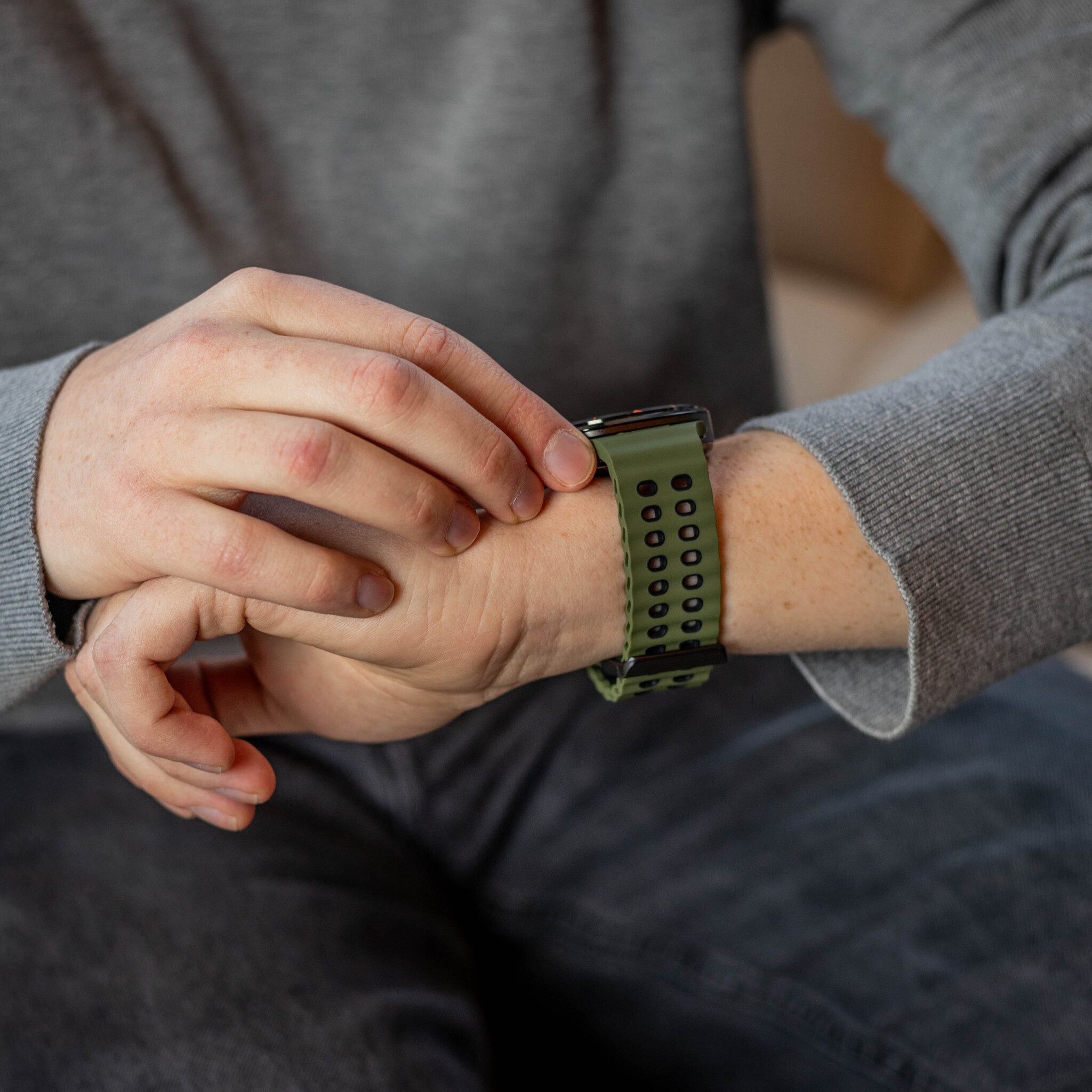 Eine Person trägt eine grüne Smartwatch und sieht auf die Uhrzeit.