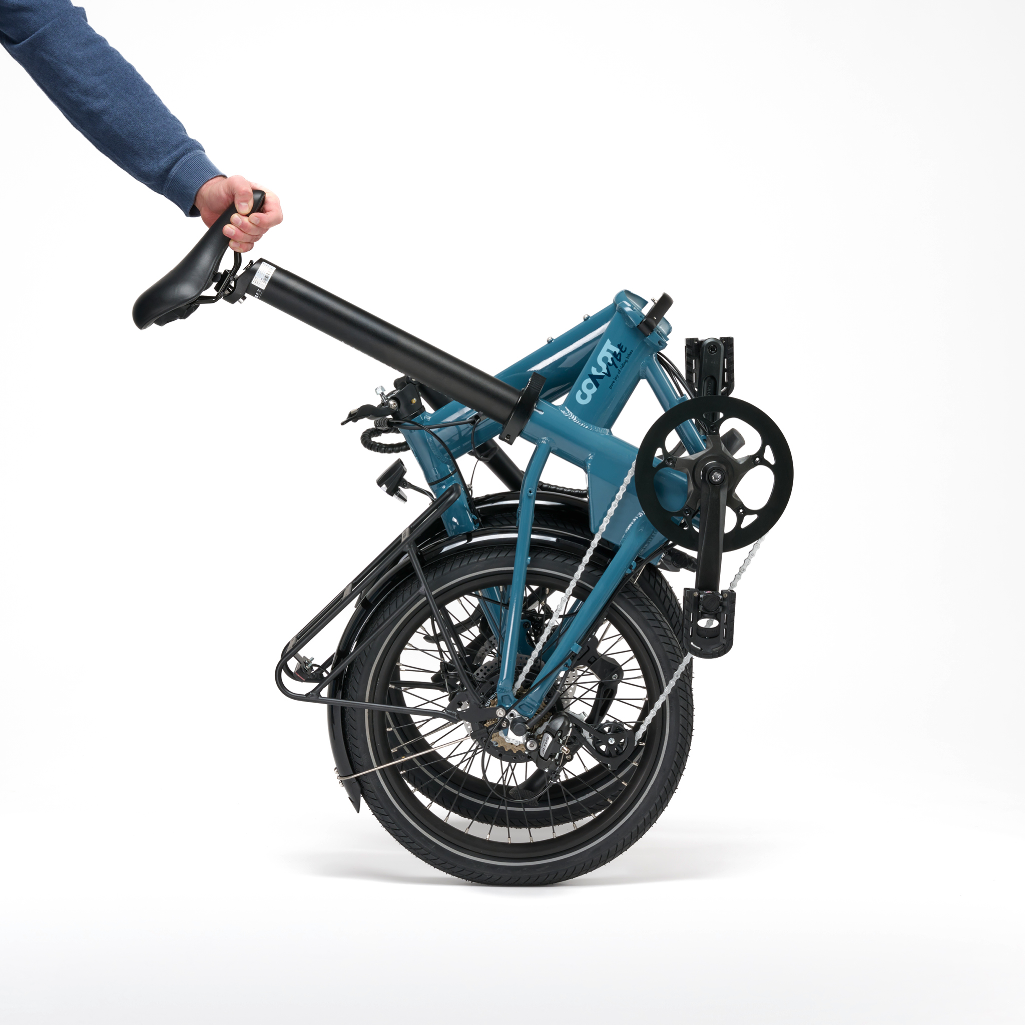 Ein faltbares blaues Fahrrad, gehalten von einer Person. Weißer Hintergrund.