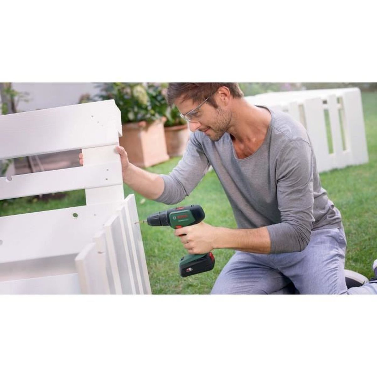 Mężczyzna używający wiertarki na białej drewnianej konstrukcji, w ogrodzie.