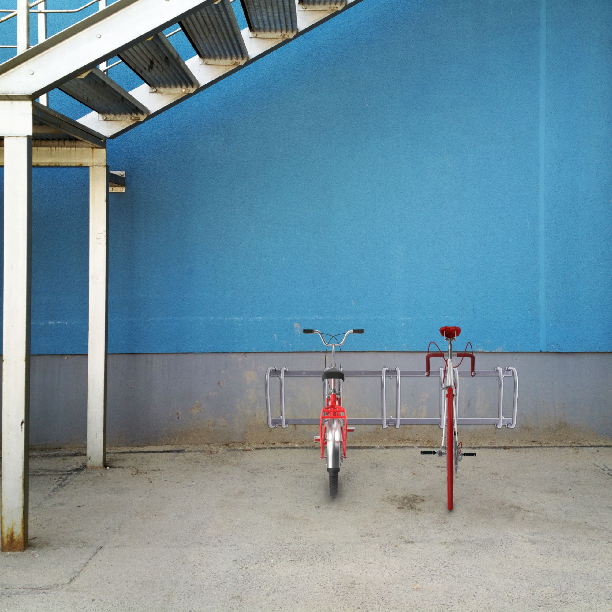 Zwei rote Fahrräder in einem Fahrradständer geparkt. Der Hintergrund ist eine blaue Wand.