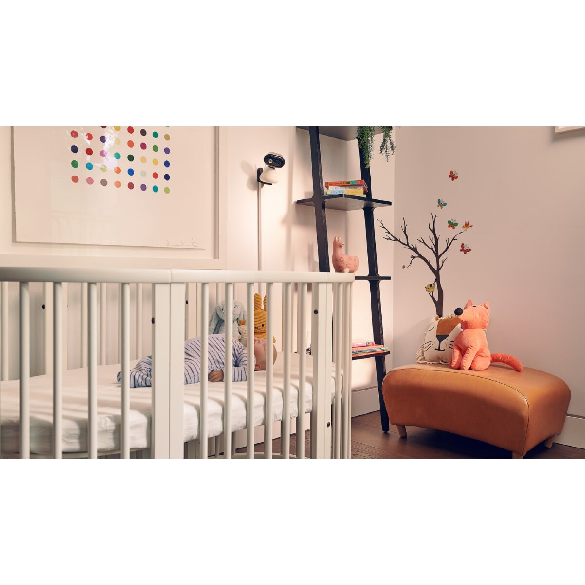 Babyzimmer mit Kinderbett, Monitor und Dekorationen. Gerahmte Kunst, Bücherregal, Fuchs-Plüschtier und Baum-Abziehbild.