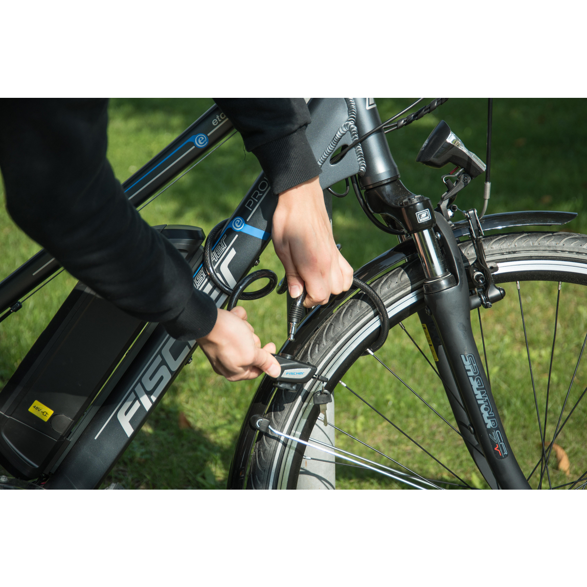 Person sichert Fahrradschloss an einem schwarz-grauen Fahrrad mit blauem Schloss.