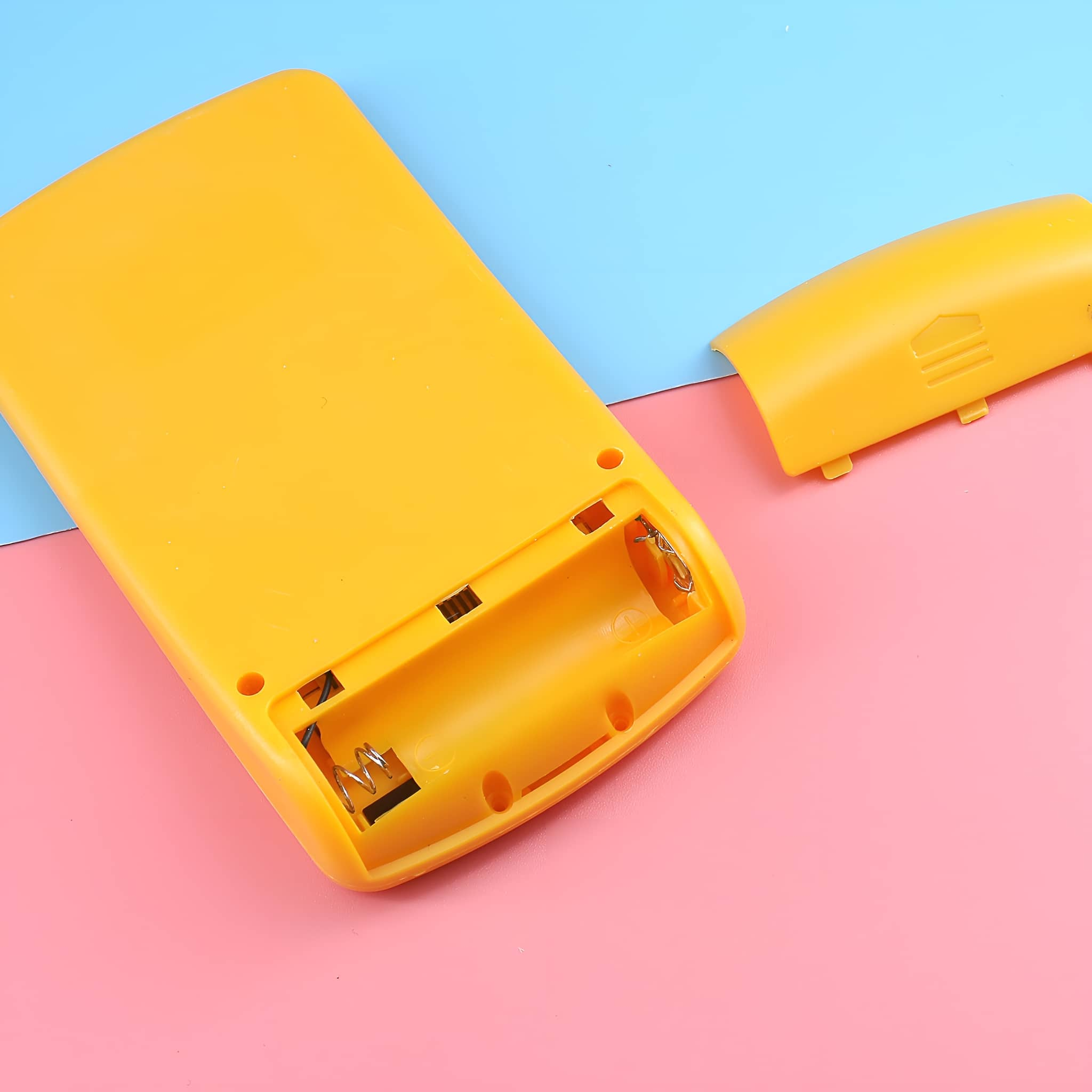 Ein gelbes Kunststoff-Batteriefach mit offenem Deckel. Der Innenraum enthält Batteriefedern.