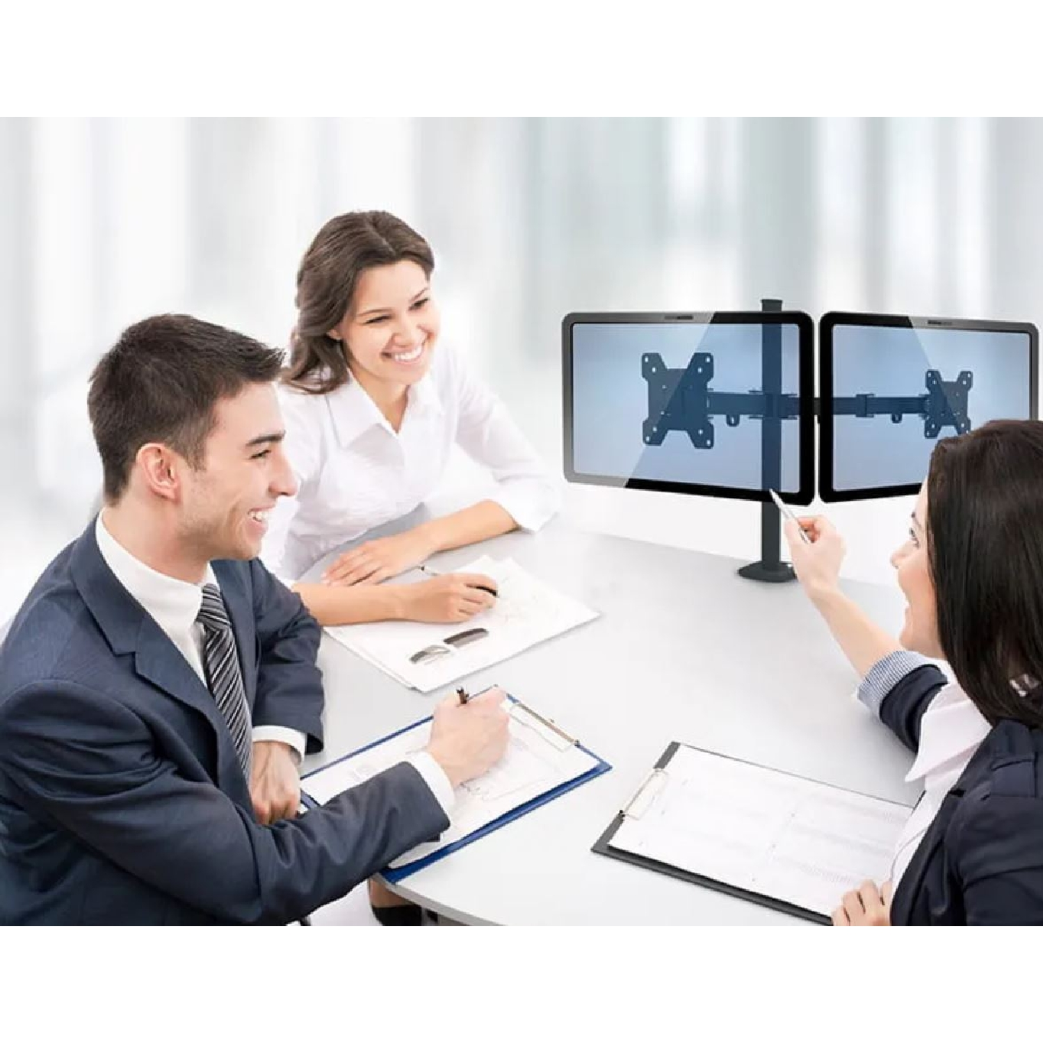 Drei Personen am Tisch diskutieren mit zwei Monitoren. Eine Person zeigt auf einen Monitor.