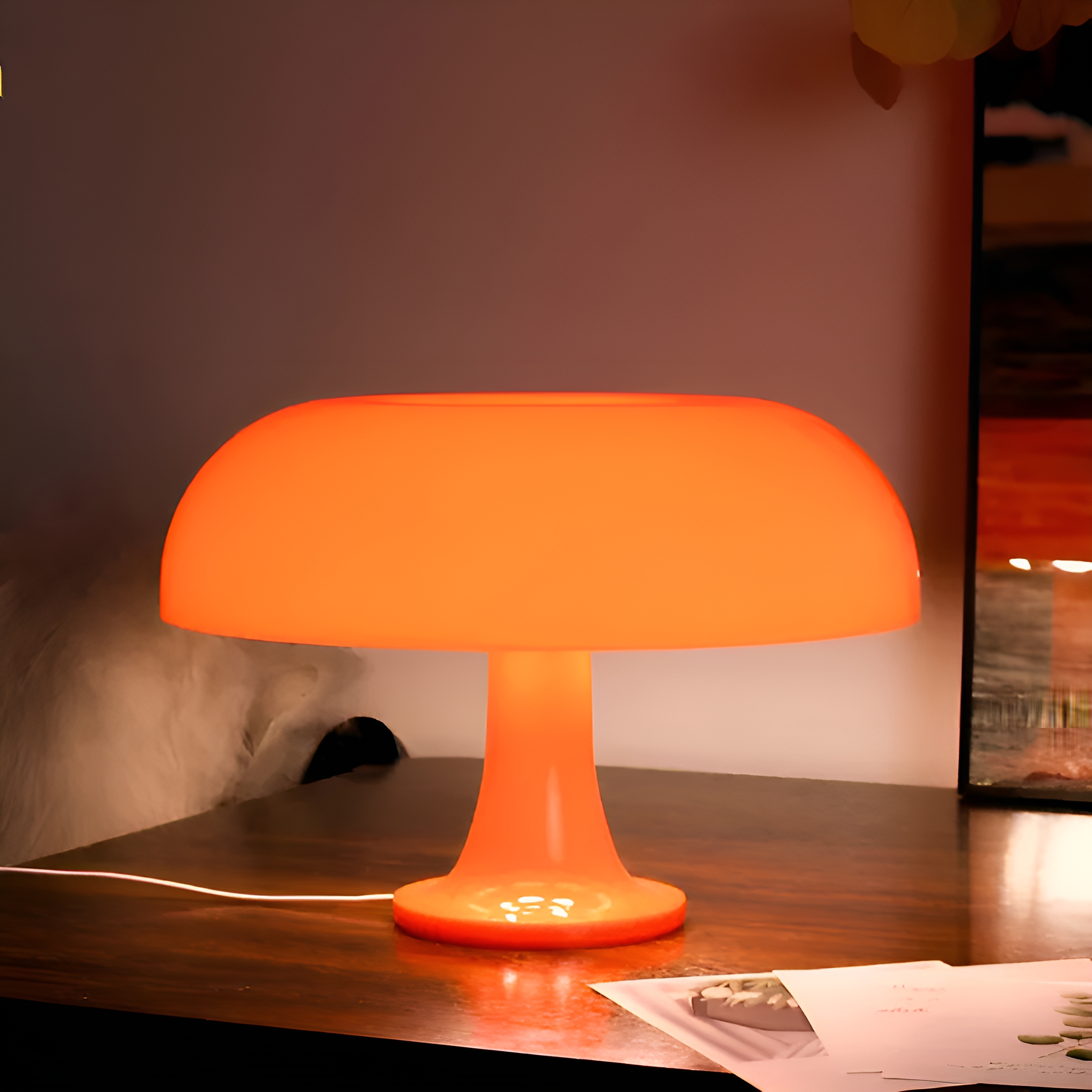 Orangefarbene Pilzlampe auf einem braunen Schreibtisch. Hintergrund ist eine Wand und ein Gemälde.